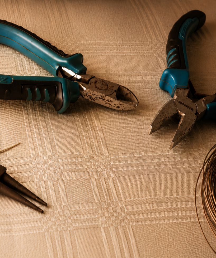 A pair of blue and black wire cutters and a pair of blue-handled pliers on a beige checkered tablecloth.