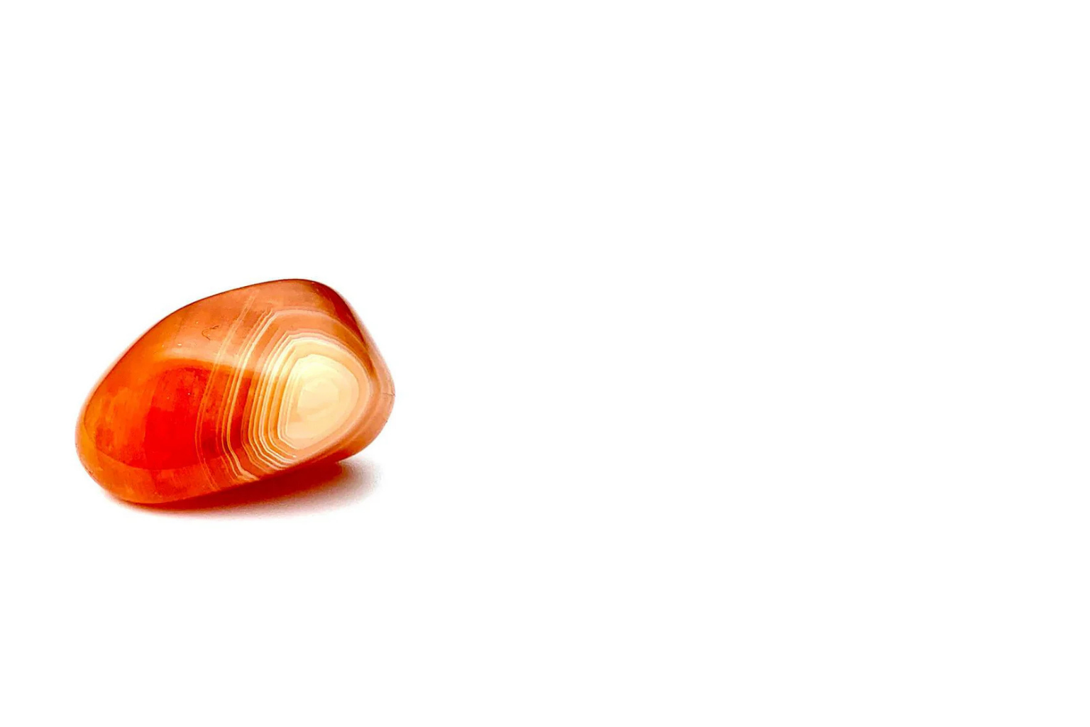 A polished orange and white banded gemstone, possibly carnelian, resting on a white surface with a plain white background.