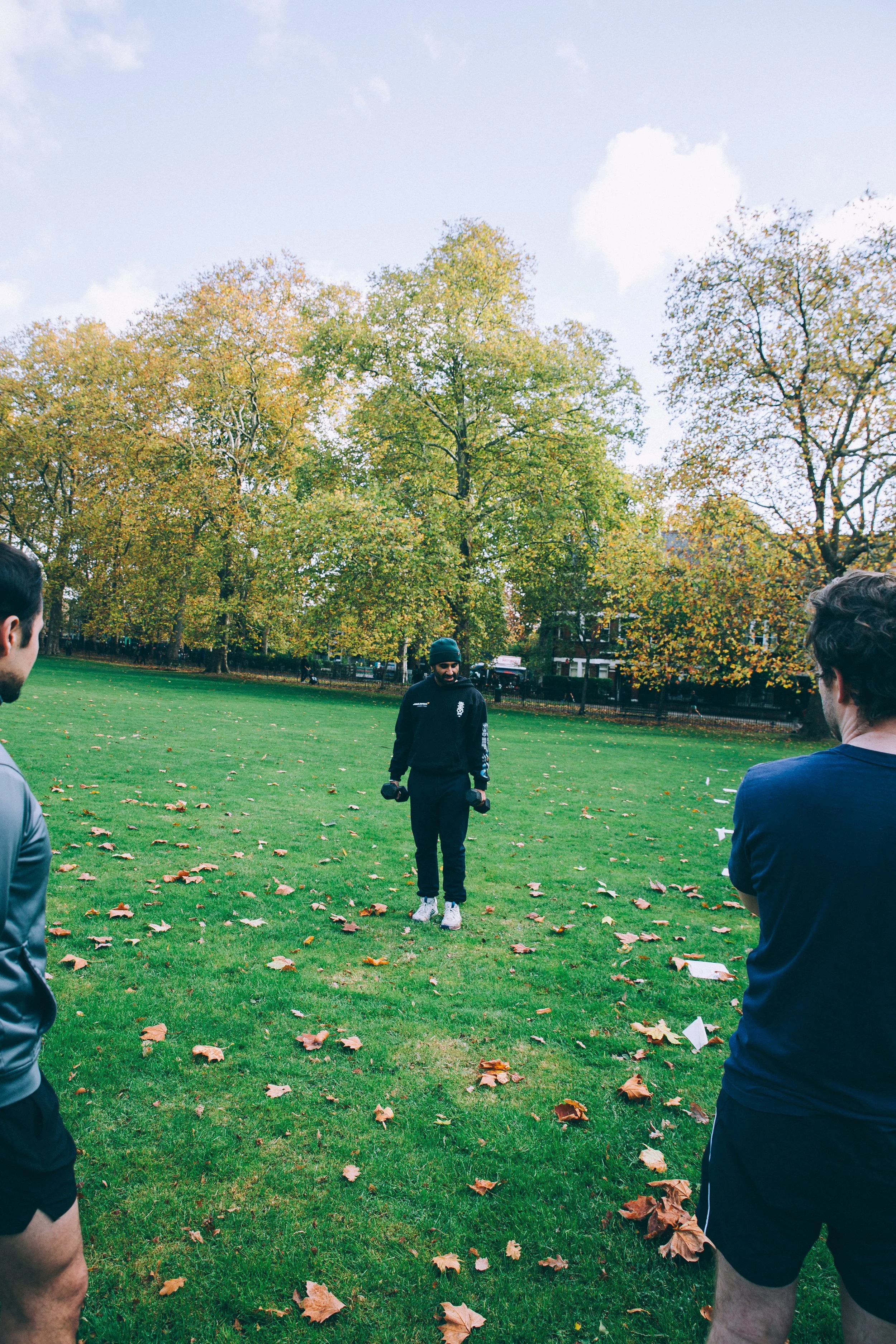 the wild LDN group coach leading the outdoor group workout with dumbbells in Highbury Fields, Islington while the participants watch on and learn carefully