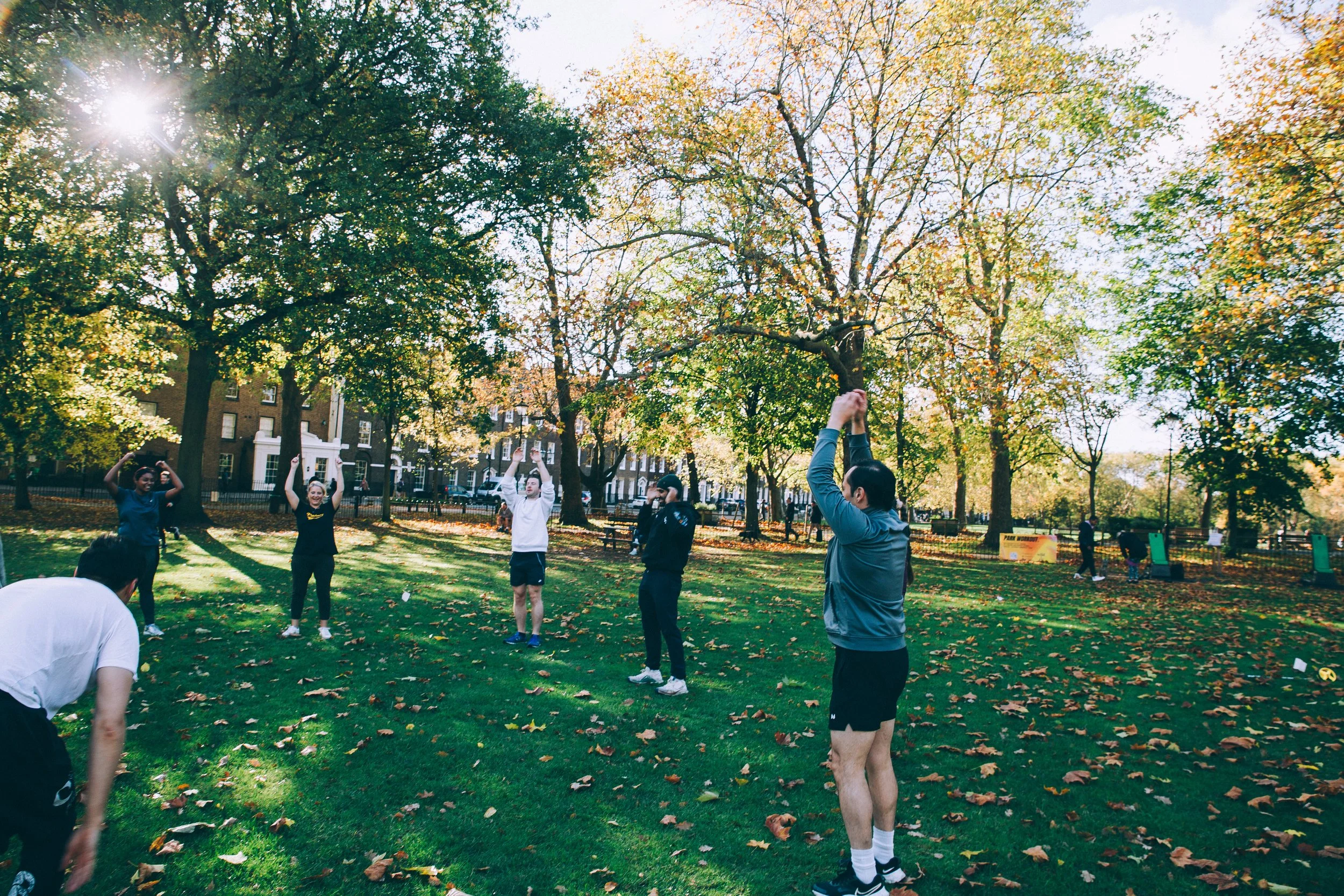 action shot during a wild LDN outdoor workout session in Highbury Fields, Islington - a group of young, athletic people in their 20s and 30s in a circle performing bodyweight movements during the outdoor fitness group class in a beautiful park. 