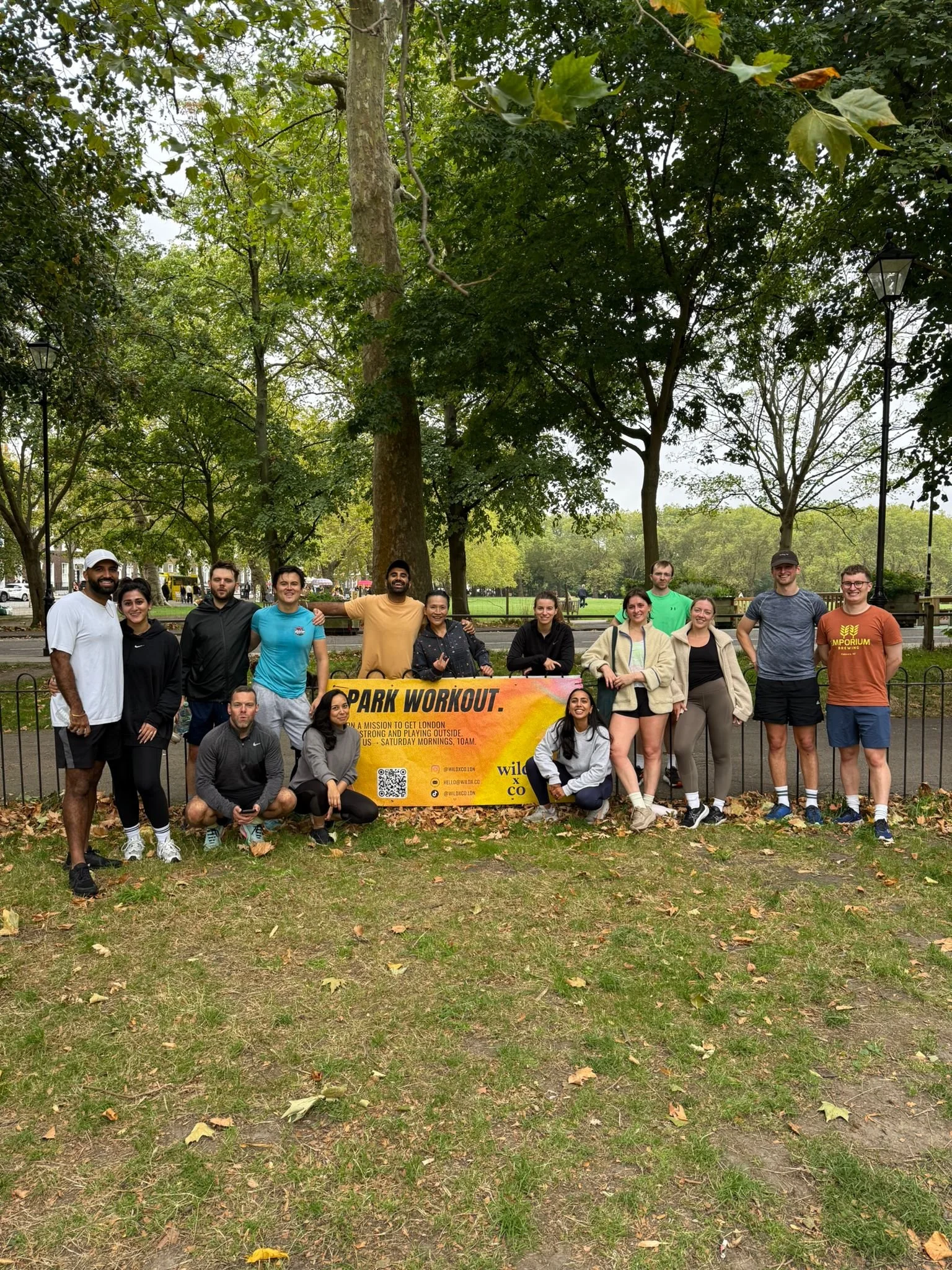post workout from wild LDN outdoor group workout in Highbury Fields, Islington - a group of young, athletic people sweaty and happy after the fitness class in a beautiful London park. yellow banner reads: "PARK WORKOUT."
