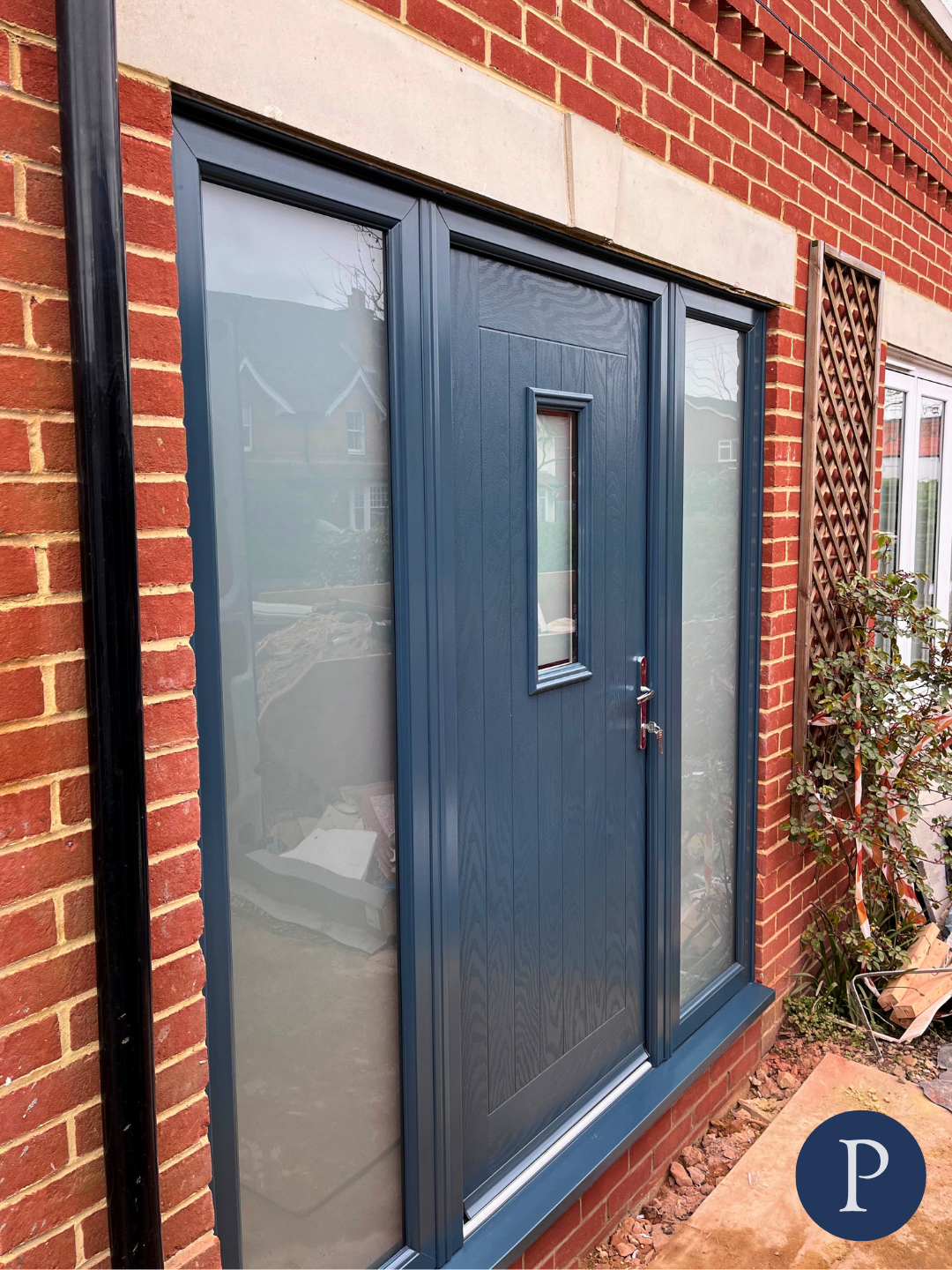 Blue front door with a narrow window in a brick house with brick and stone accents.