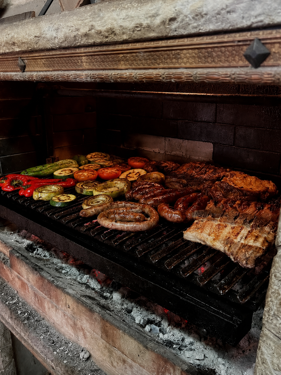 Asados con verduras y carnes en una parrilla de piedra.