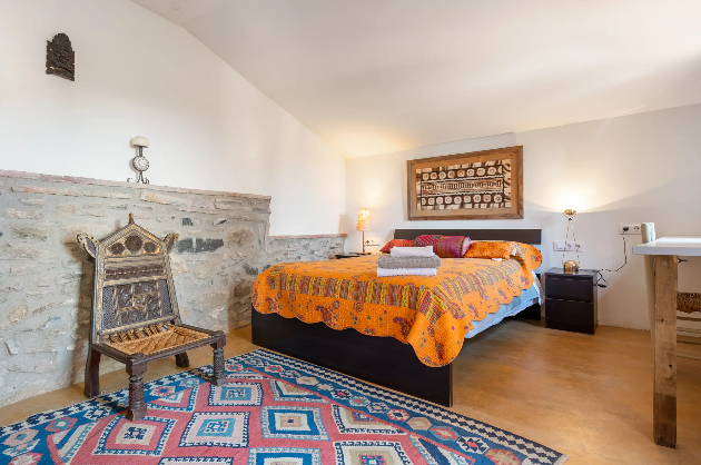 Habitación con cama de matrimonio, colcha de colores cálidos, alfombra colorida y decoración tradicional en las paredes.