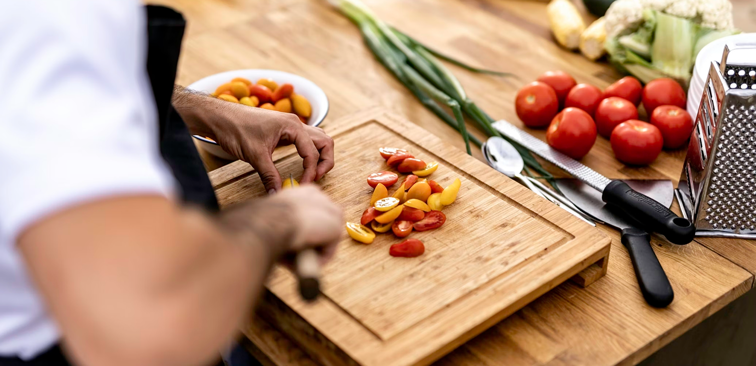 Persona cortando tomates cherry en una tabla de cortar de madera en la cocina.
