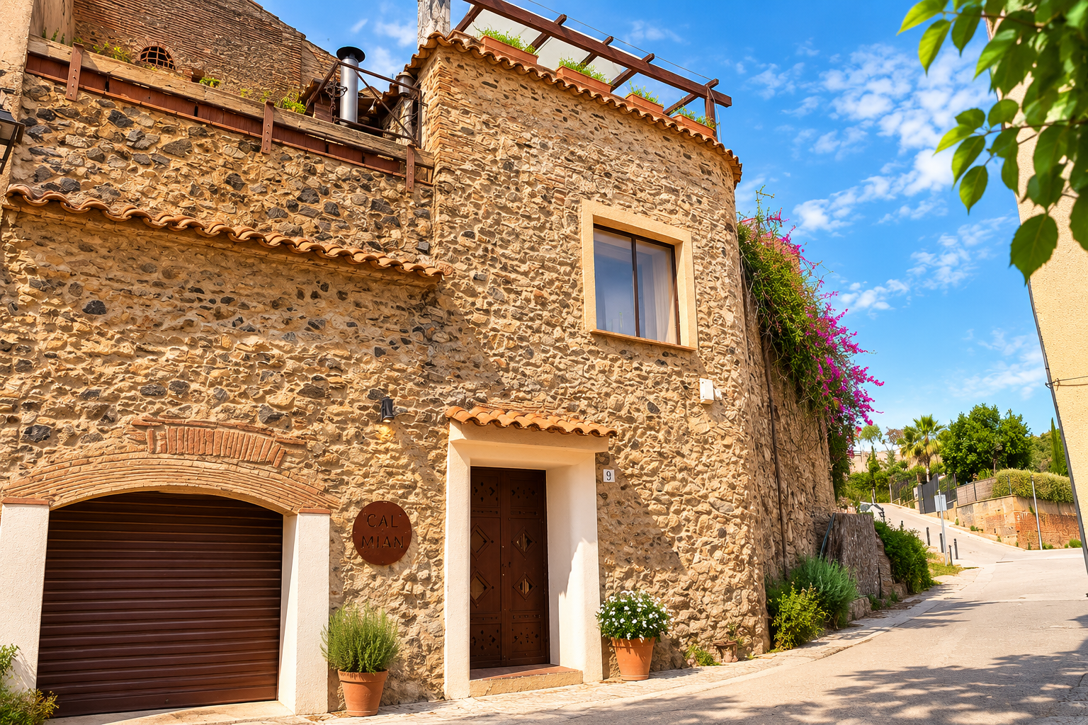 Casa de piedra con puerta de madera, una ventana y plantas en macetas en la entrada, en una calle con vegetación y cielo azul