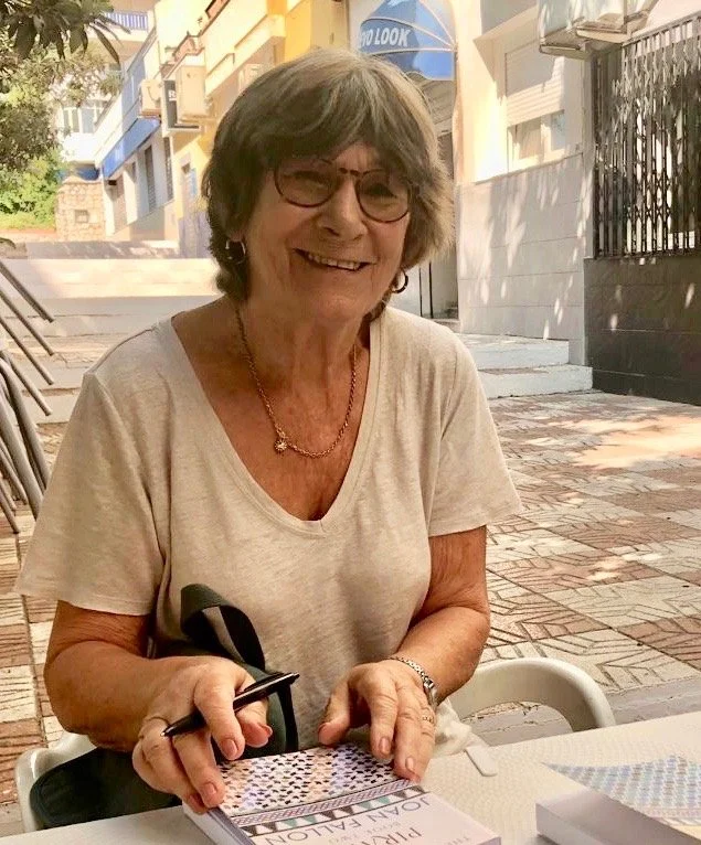 Joan Fallon sitting in the sunshine signing copies of her books.