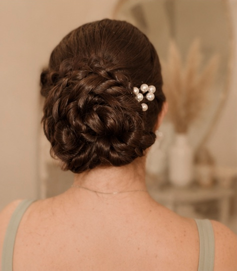 Back view of a woman with an elegant braided updo hairstyle adorned with pearl hairpins.
