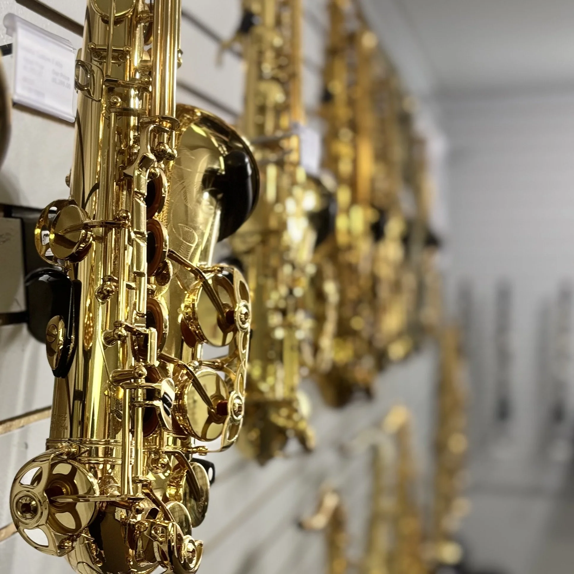 A row of shiny gold-colored saxophones hanging on a wall, with focus on the closest instrument.