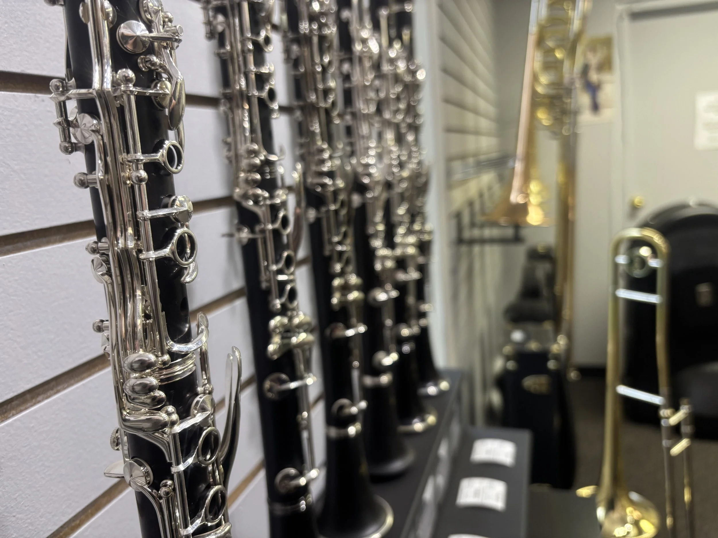 A display of multiple musical instruments, specifically flutes and saxophones, arranged on a wall in a music store.