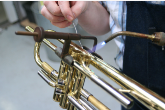 Person welding a brass instrument, possibly a trumpet, with a blowtorch.