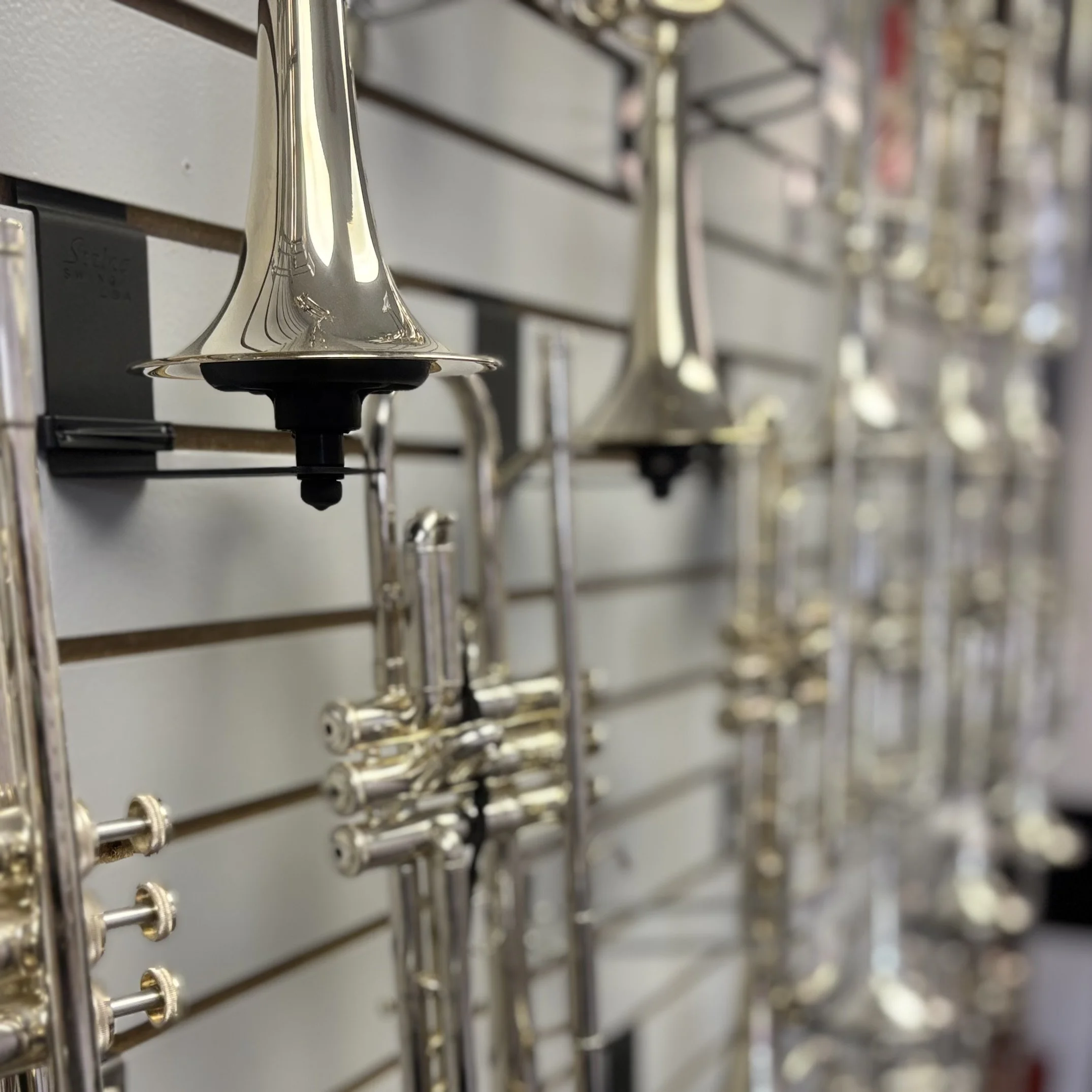 Close-up view of shiny silver saxophones hanging on a display wall.