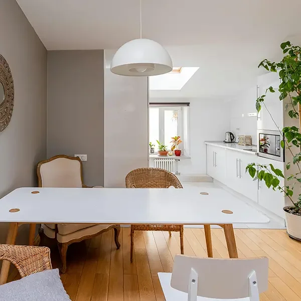 Bright kitchen and dining area with white cabinets, wooden floor, and a white table with various chairs.