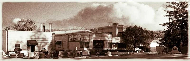 Historical black and white photograph of a small town with a building labeled 'Bell Memorials' and numerous graves in the cemetery in front.