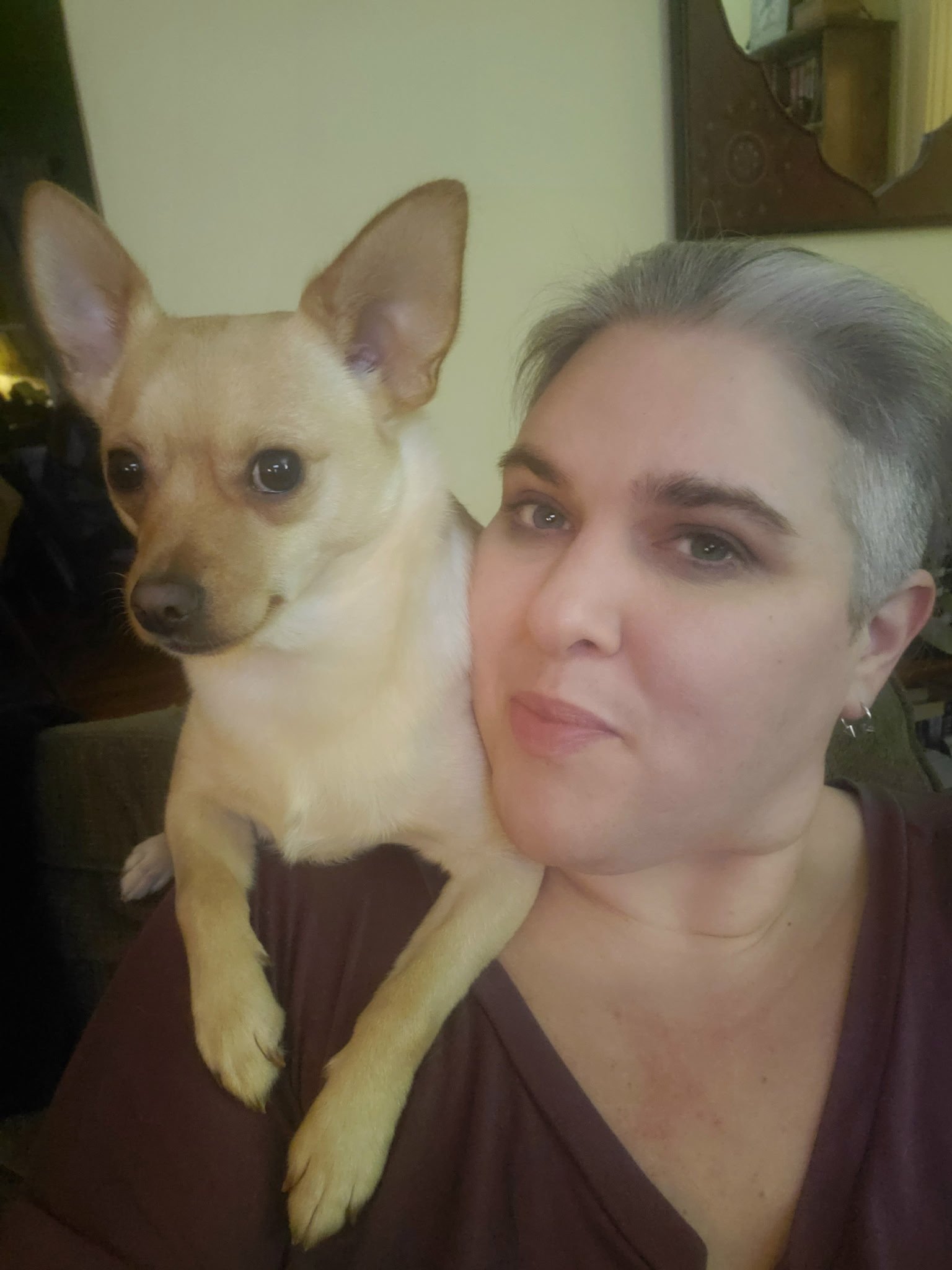 A person with gray hair taking a selfie with a tan and white dog with large ears, both looking at the camera.