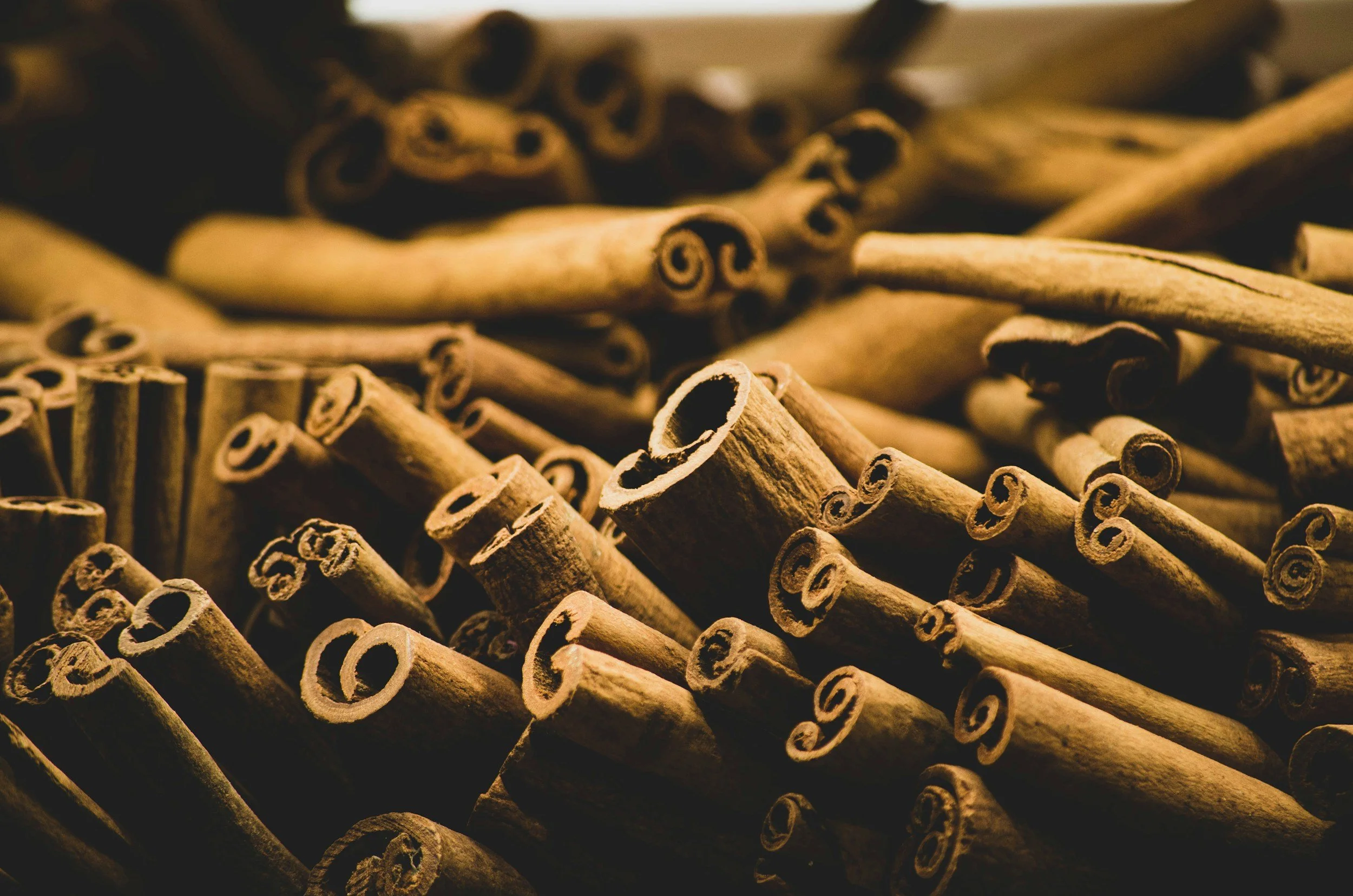 Close-up of cinnamon sticks piled together, displaying their curled shape and textured surface.