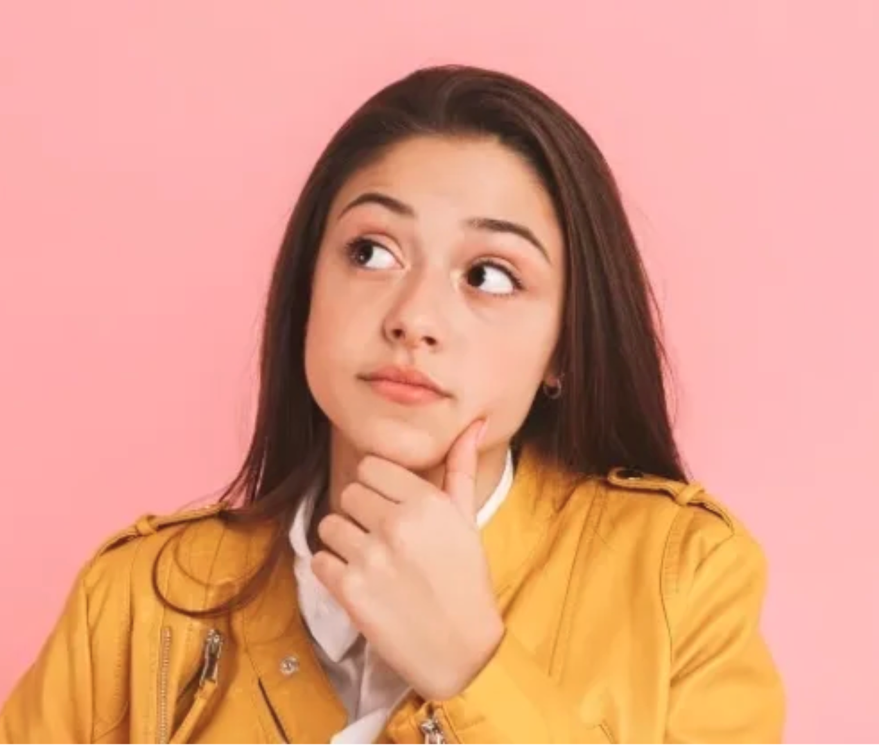 Young woman with dark brown hair and yellow jacket, posing thoughtfully against a pink background.