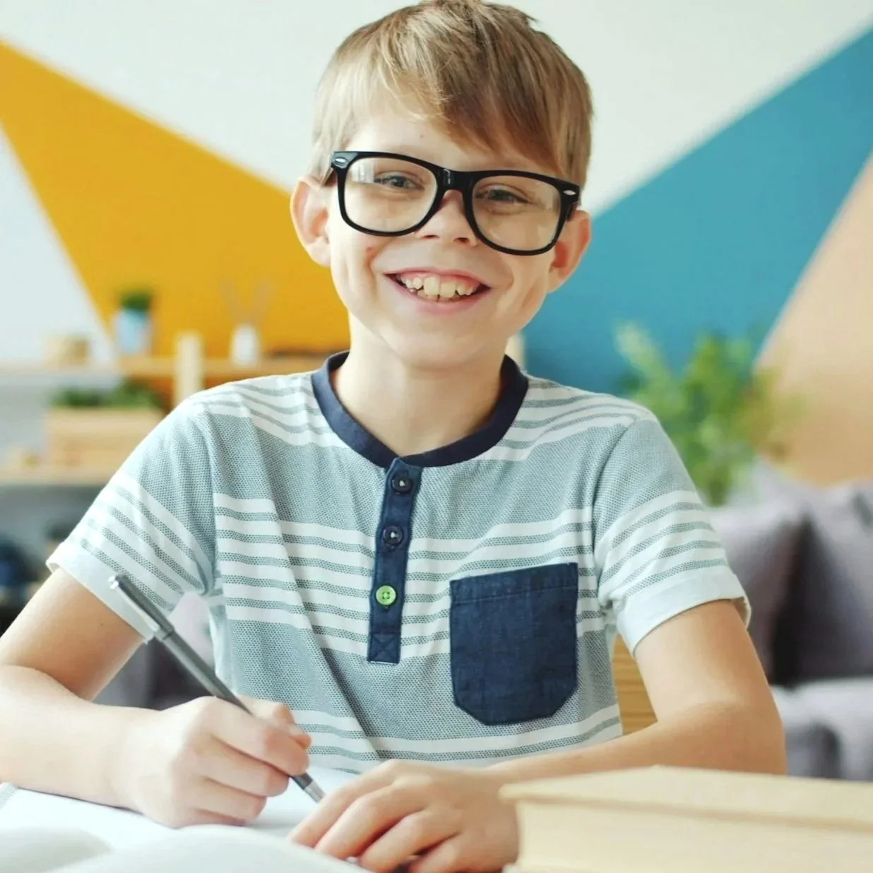 Smiling tween boy with glasses writing at a desk — engaged in critical thinking and problem-solving activities for kids