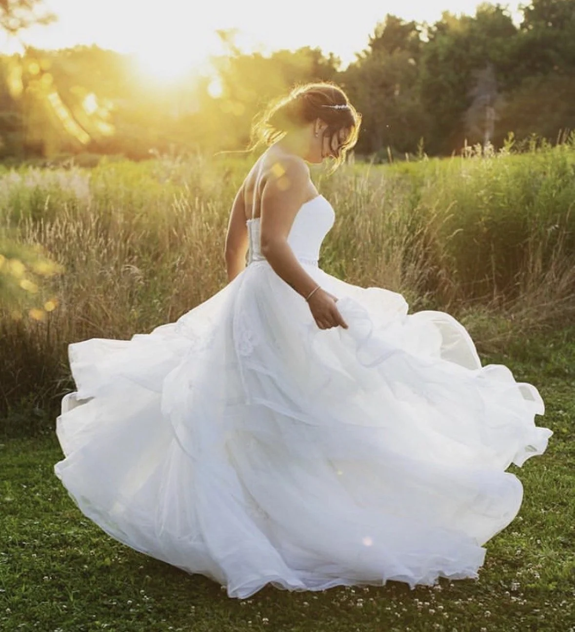 A bride in a white wedding dress walking through a field at sunset golden hour.
