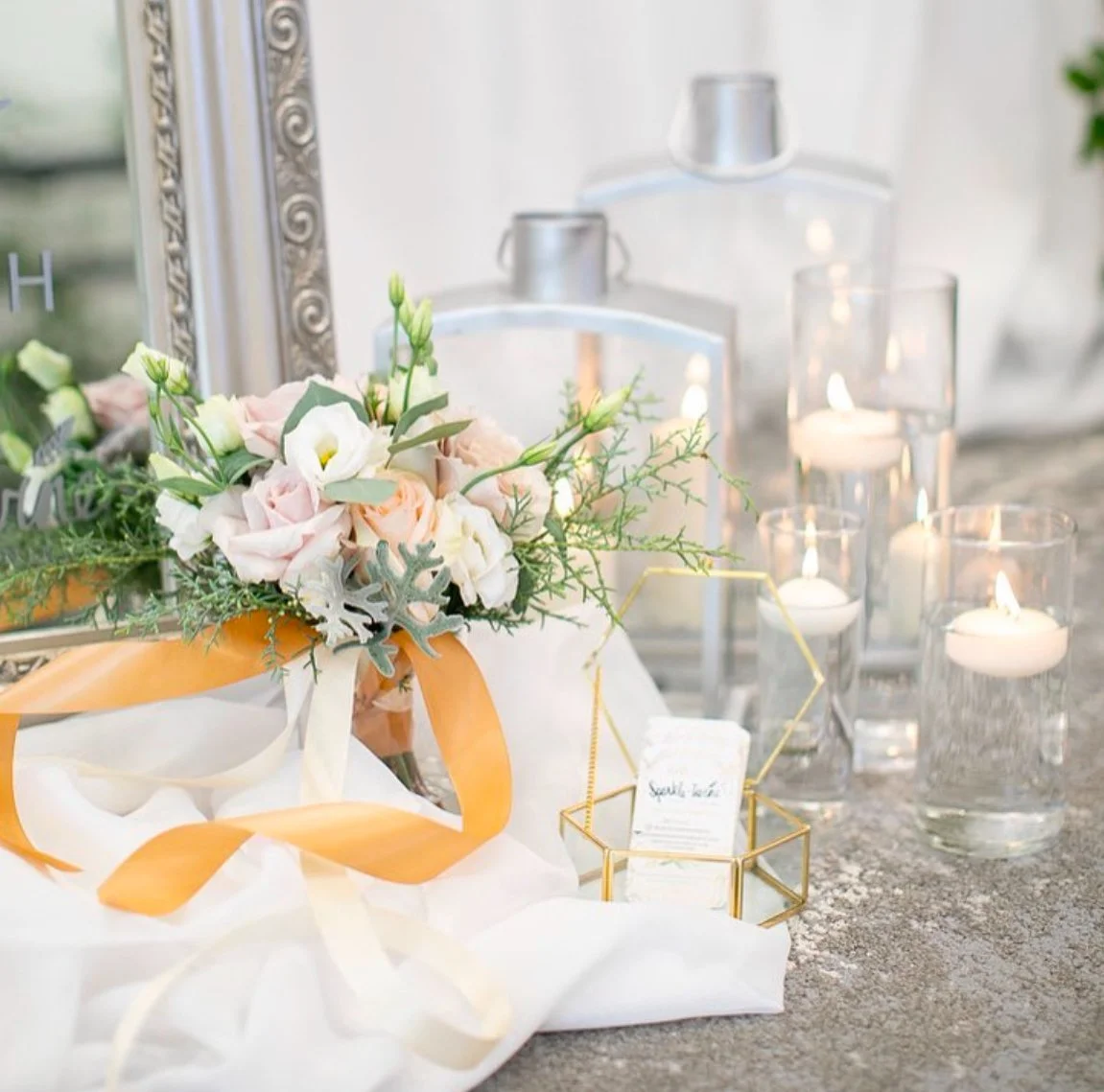 Elegant table setting with a floral bouquet, tea light candles, and a geometric gold holder on a gray table.