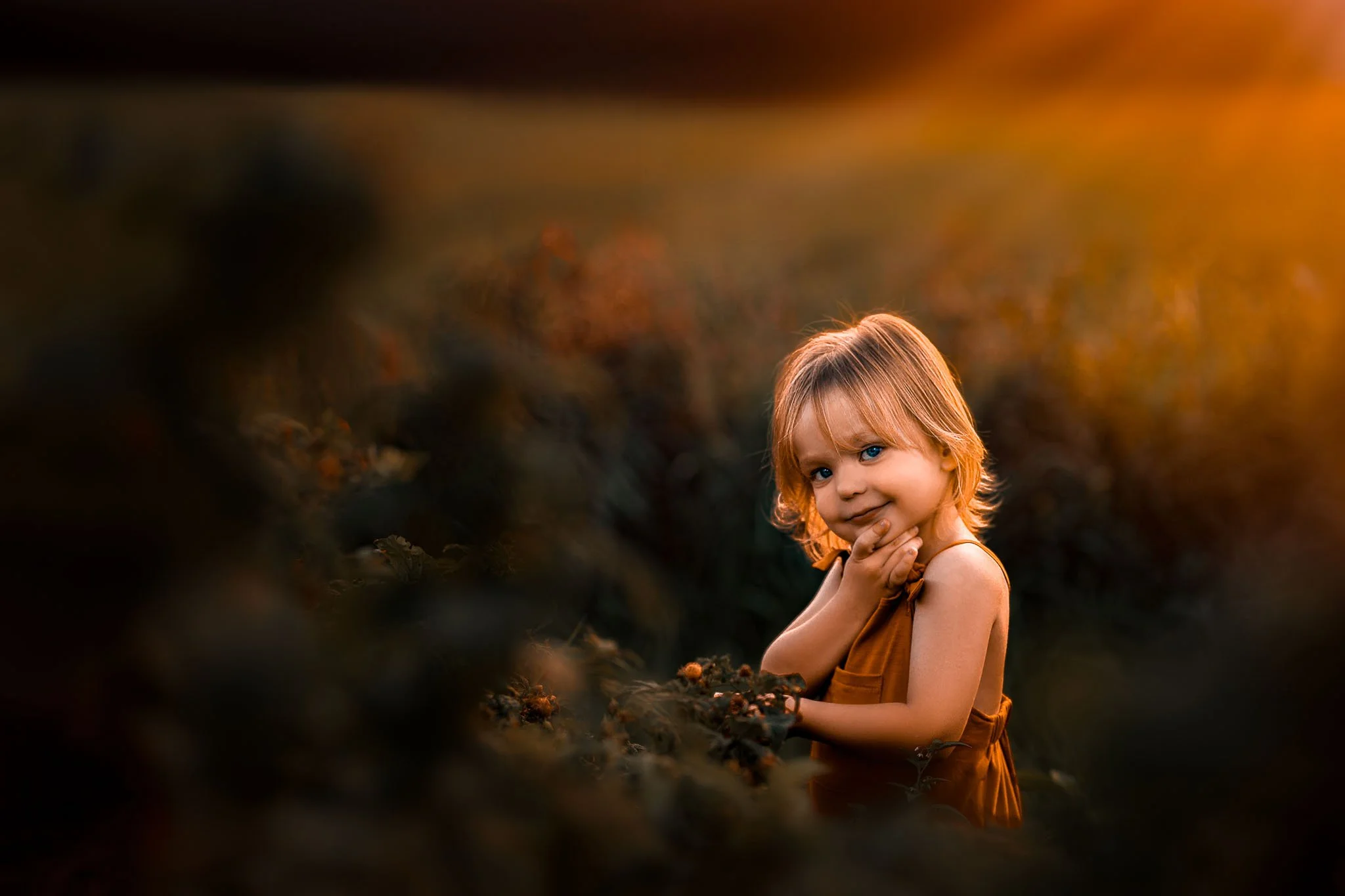 A young girl with blonde hair and blue eyes smiling in a field during golden hour.