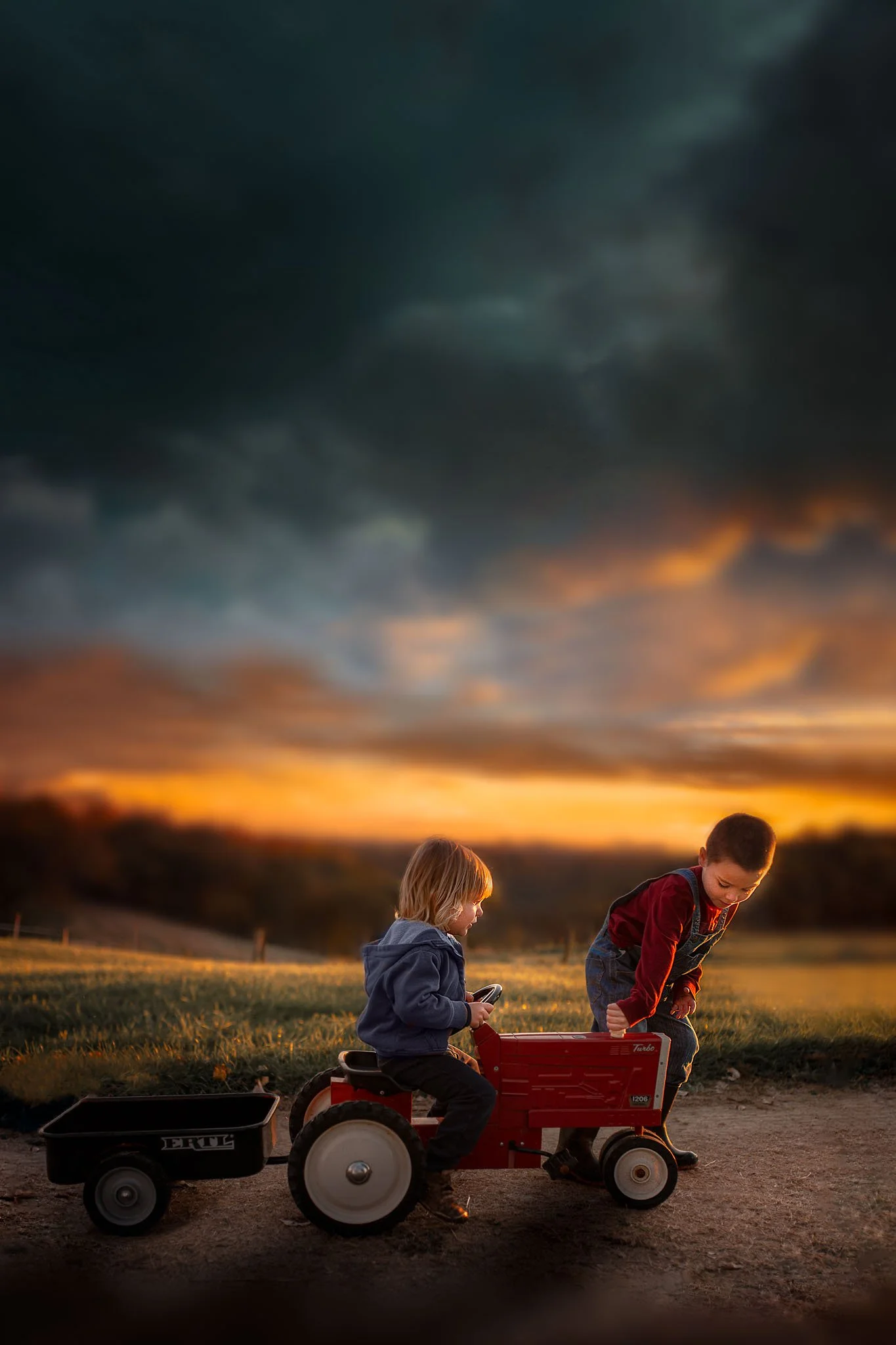 Two children playing with a red tractor toy outdoors during sunset, with a dark cloudy sky in the background.