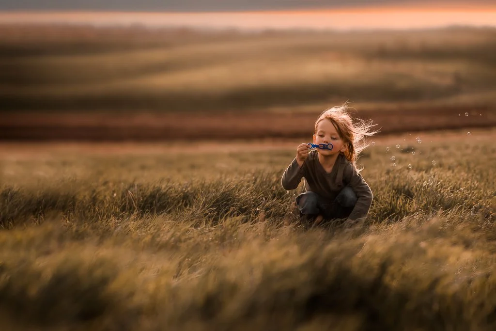 A young girl playing with bubbles in a field during sunset.