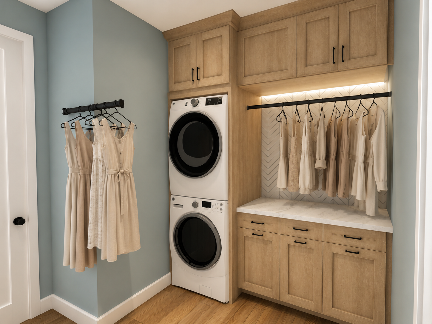 A laundry room with light wood cabinets, a marble countertop, and light blue walls. There is a stacked washer and dryer next to a small hanging rod with beige dresses, and a larger rod with more beige clothing.