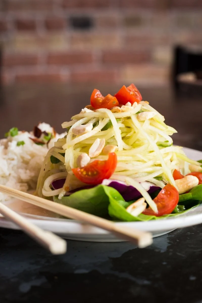 A plate of mango salad topped with cherry tomato halves, with chopped nuts and fresh greens underneath.