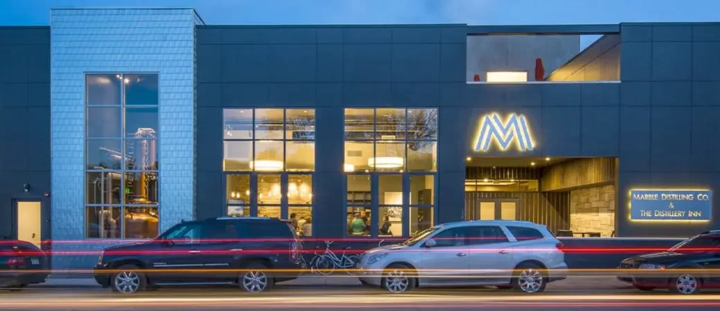 Photo of a modern brewery and distillery with cars parked in front, illuminated sign shows 'MABIE DISTILLING CO & THE DISTILLERY INN'
