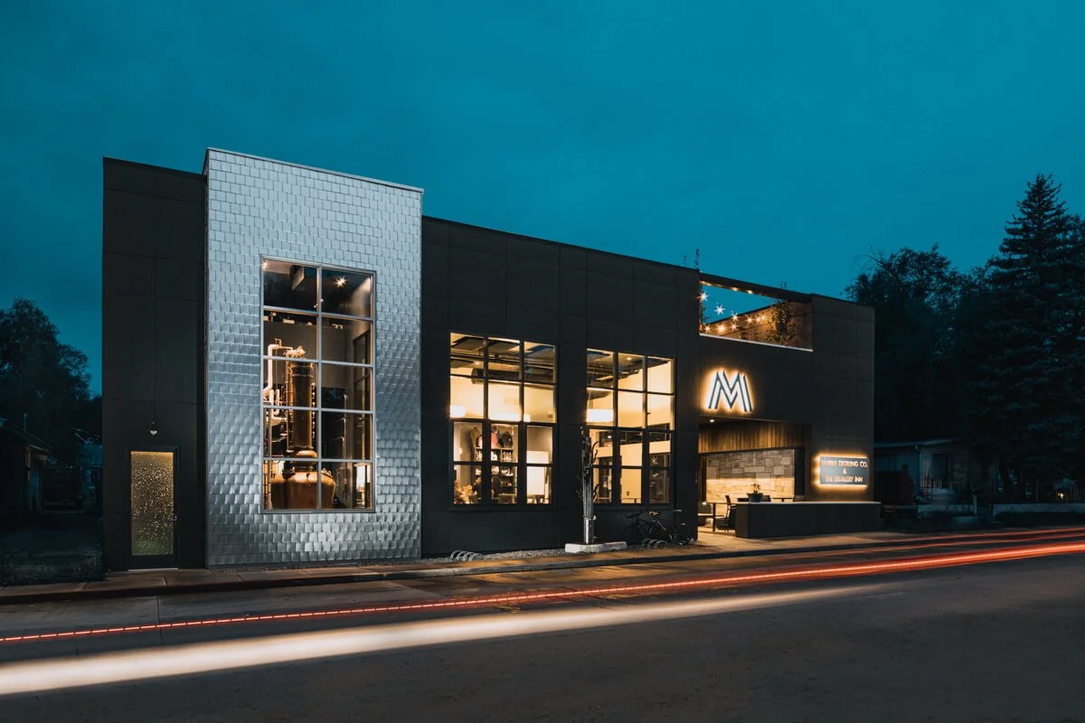 Modern commercial building at dusk with large illuminated windows, a metallic textured facade, and neon signage.