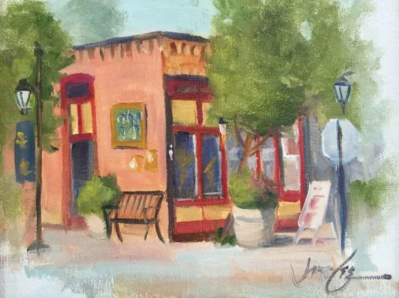 Painting of a colorful storefront with windows, a bench, street lamps, trees, and an easel outside.