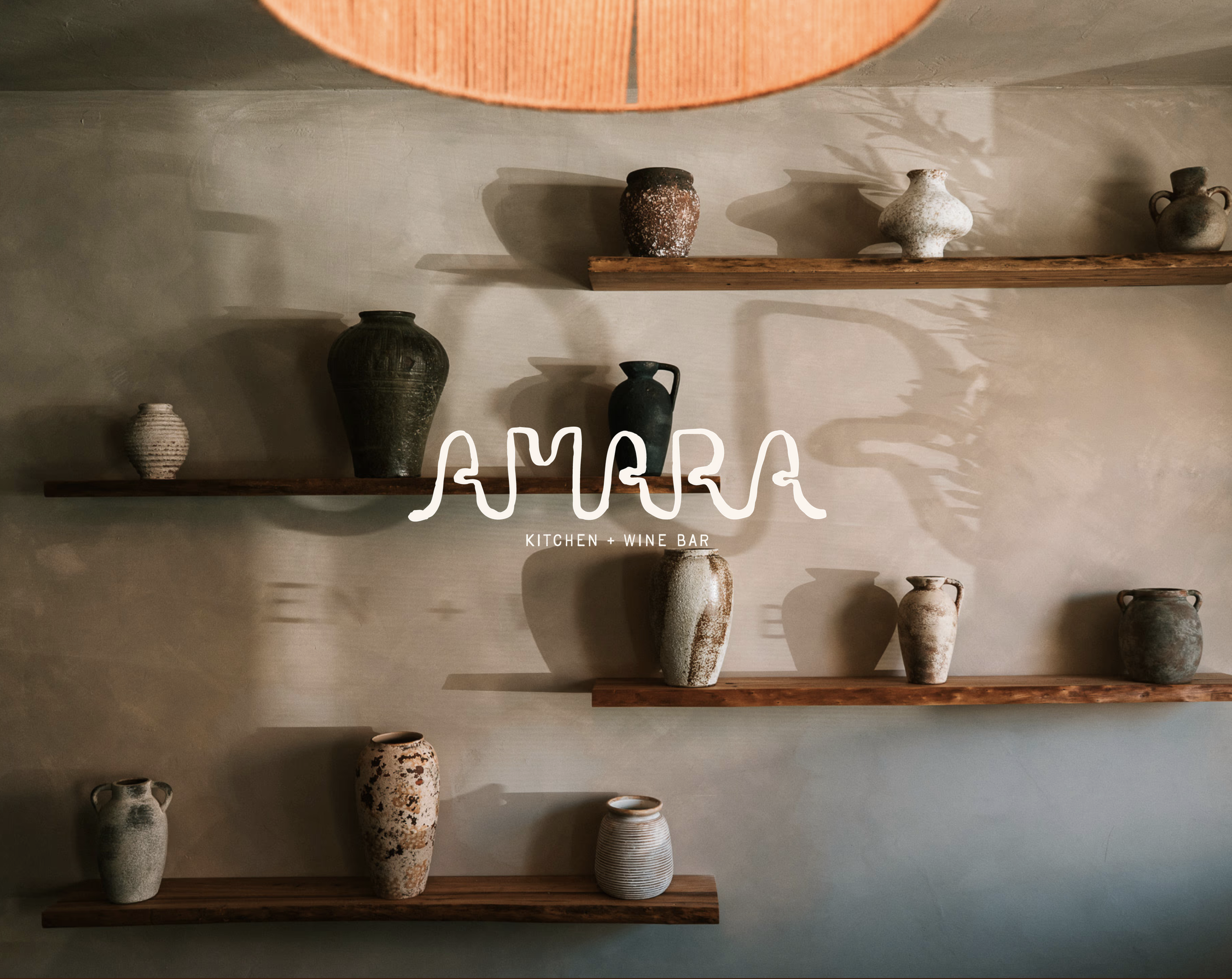 A display of ceramic vases and pottery on wooden shelves against a beige wall, with a partially visible pink lampshade at the top.