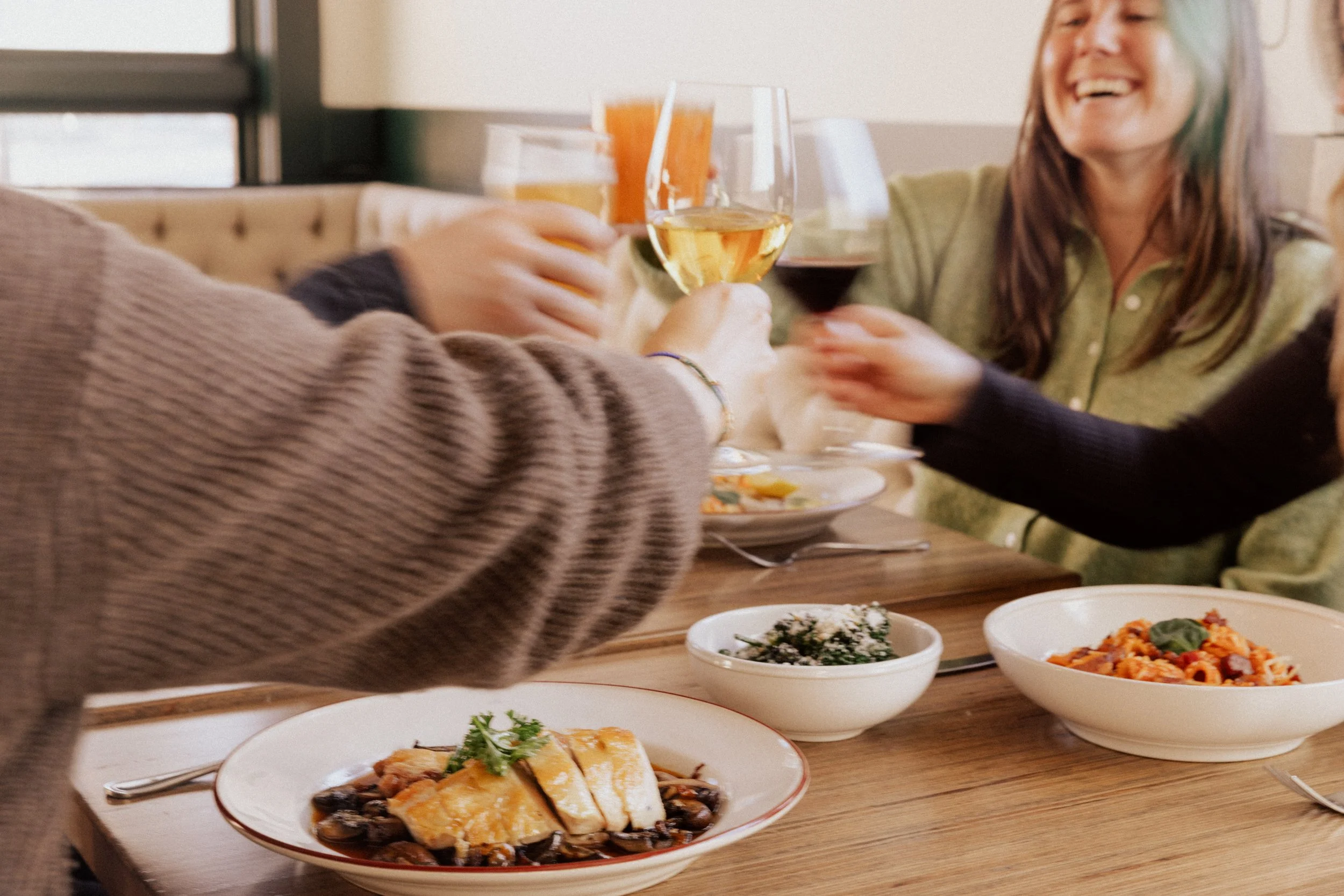 People raising glasses of wine and orange juice in a toast at a dining table with various dishes.
