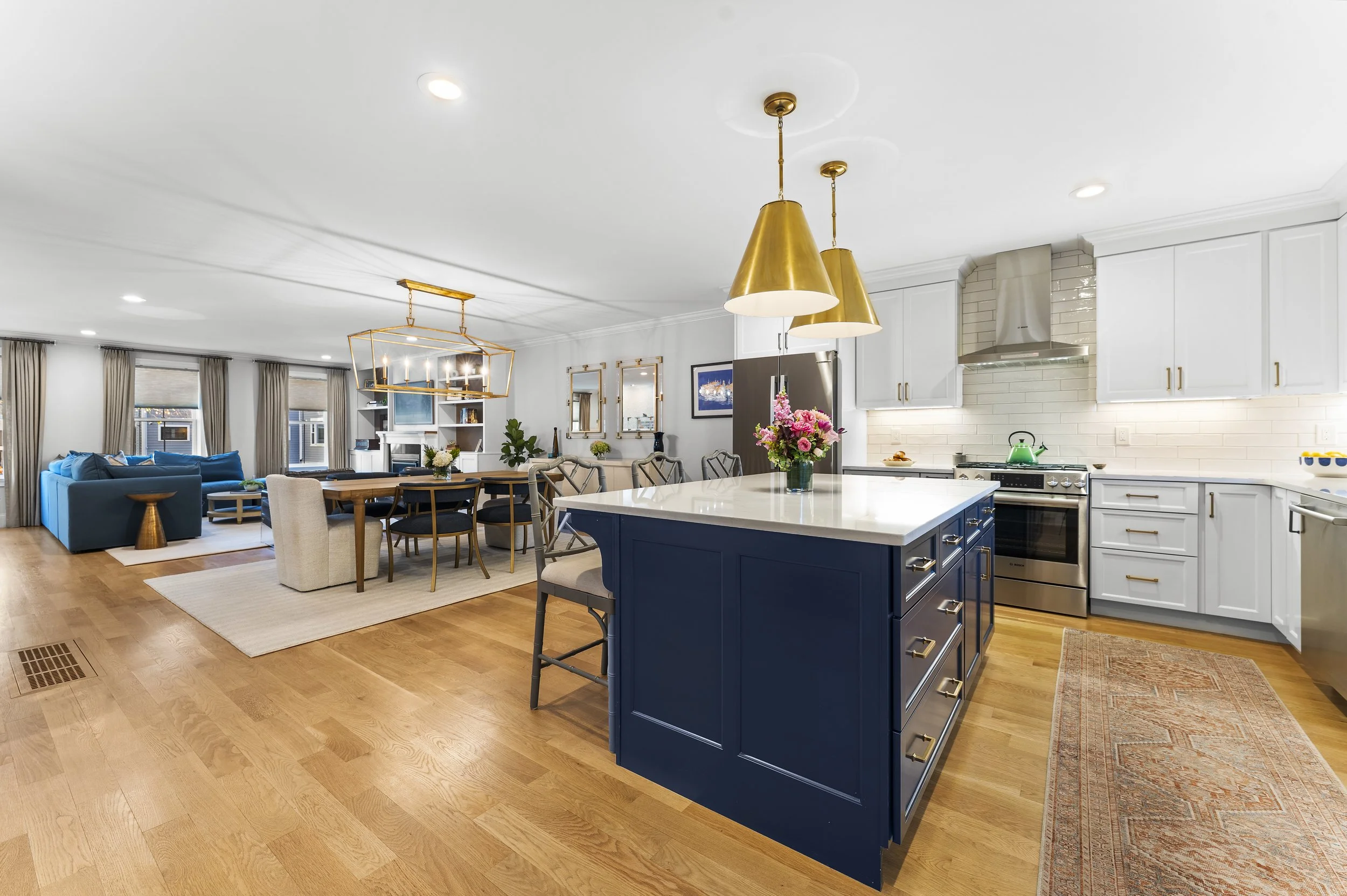 Open-concept living room and kitchen with hardwood floors, white cabinets, a blue kitchen island, and gold pendant lighting.