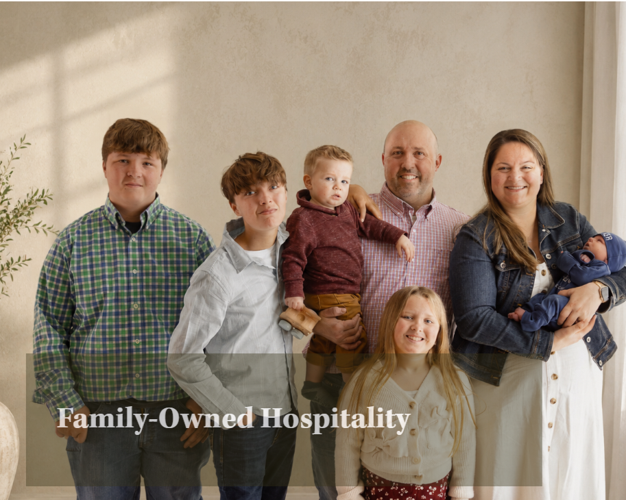 Family standing together in a room, with a woman holding a newborn baby, a man and children smiling, and a plant visible on the left. The text overlay reads 'Family-Owned Hospitality'.