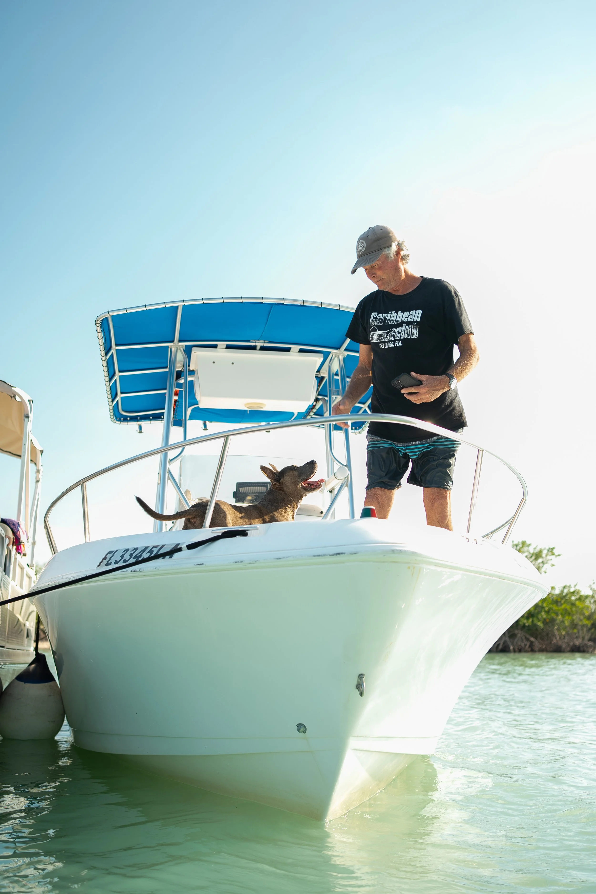 A man and a dog on a white boat with a blue canopy, on calm water during daytime.