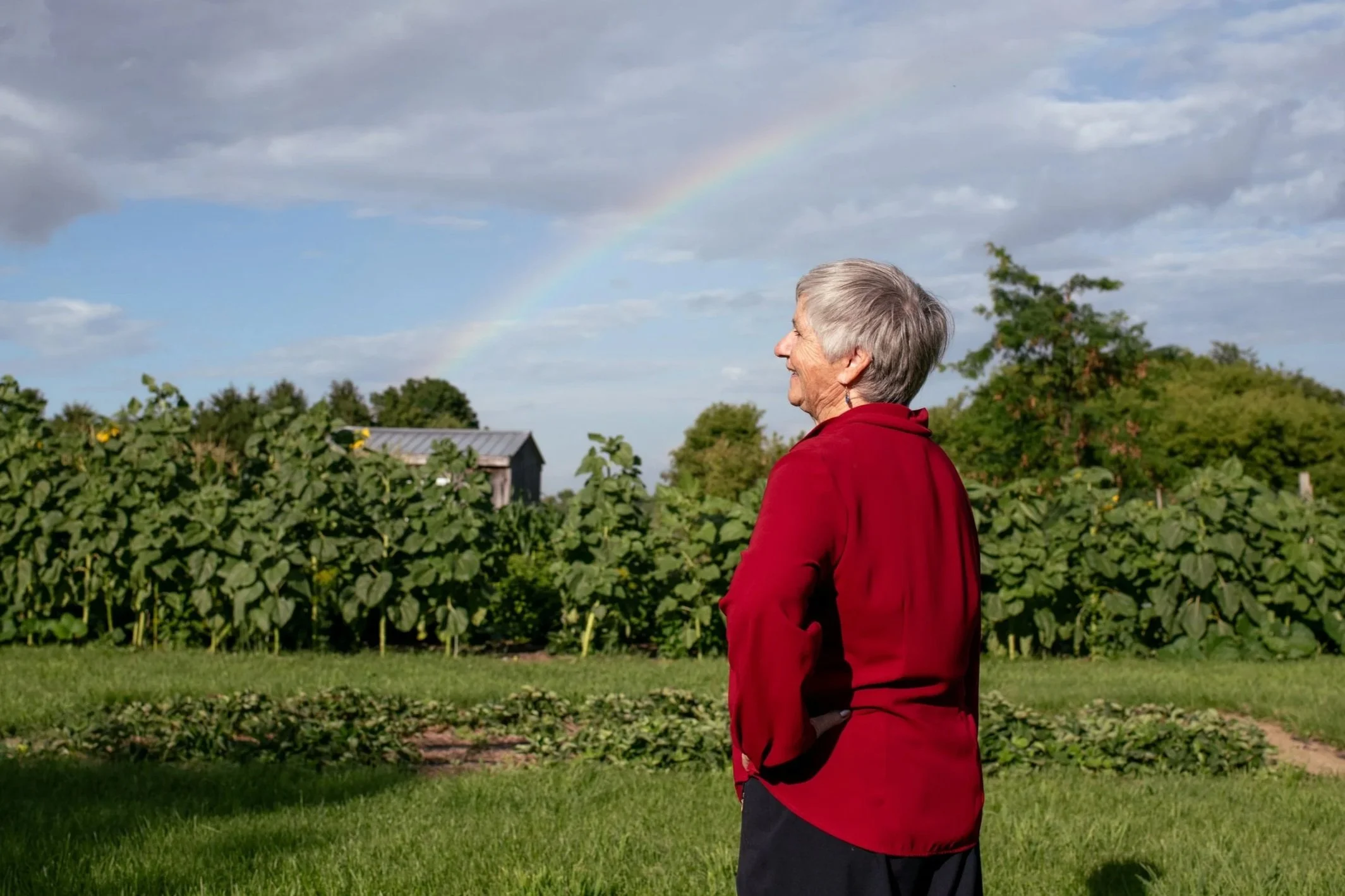 Theresa Bergeron standing in a garden, looking at a rainbow in the sky.