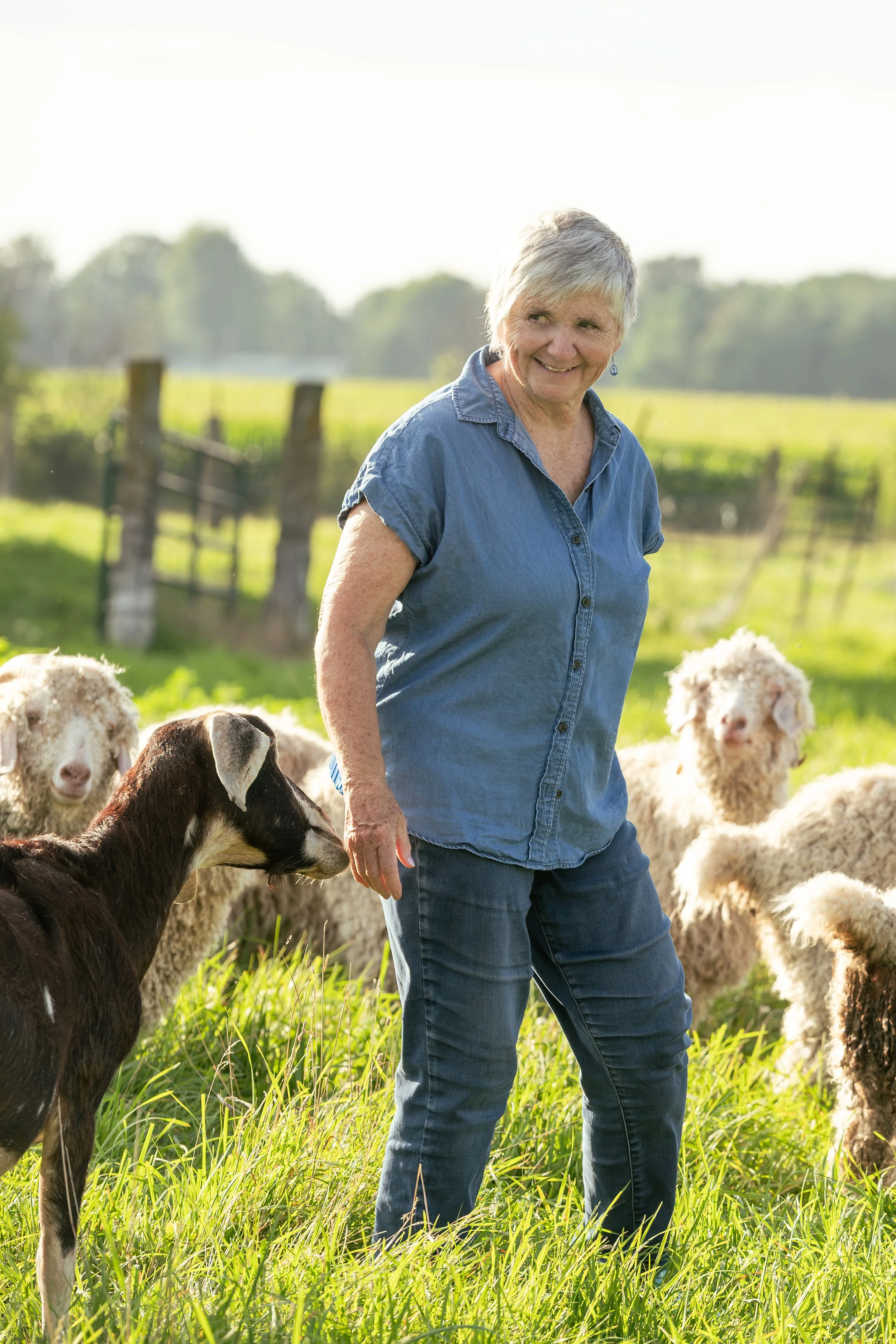 Theresa Bergeron standing in a grassy field with her goats.