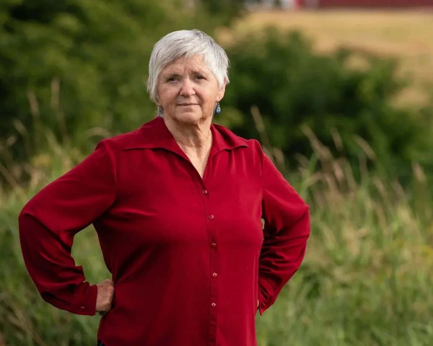 Theresa Bergeron, standing in a field with green foliage and a farm landscape in the background.