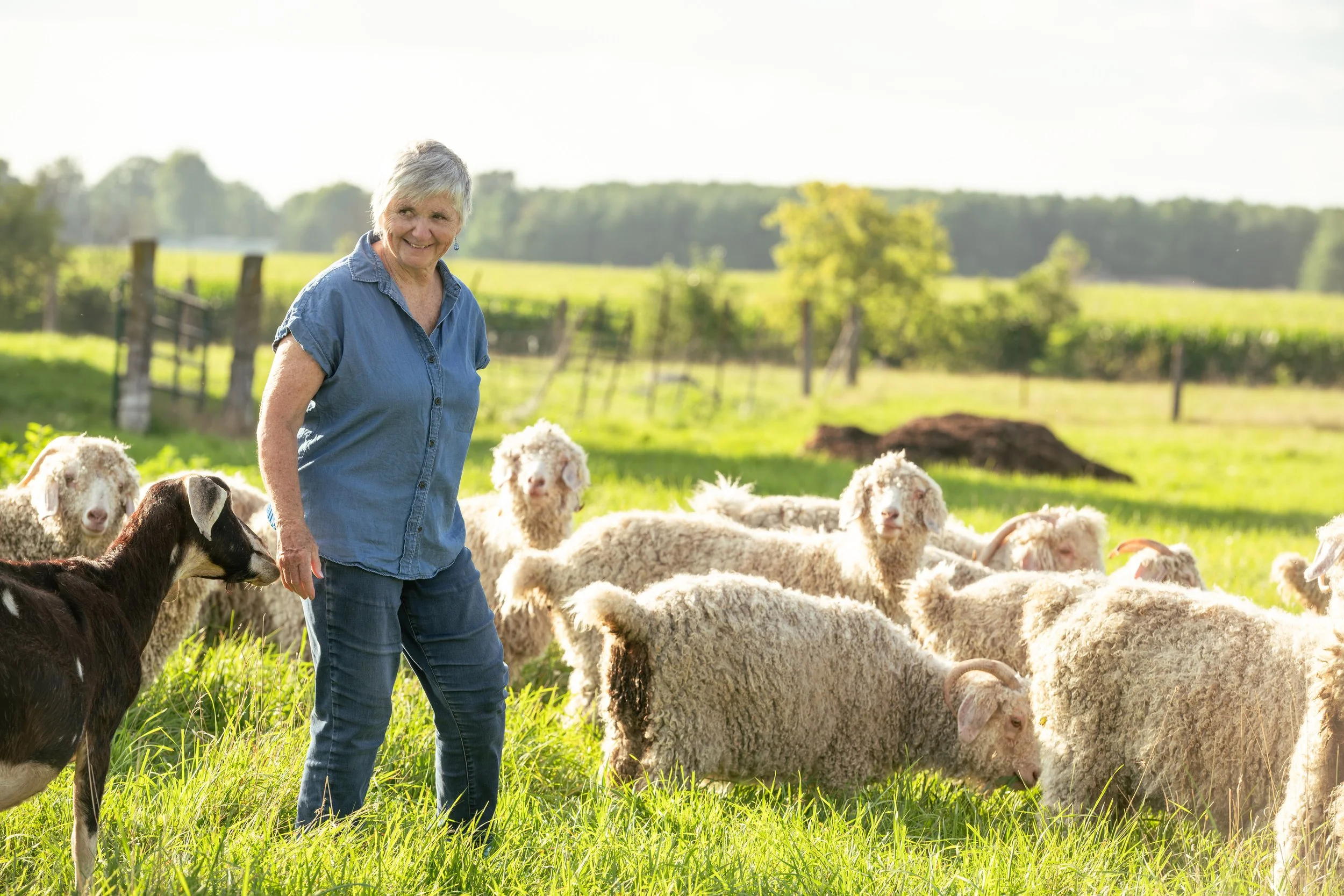 Theresa Bergeron standing in a grassy field with her goats.