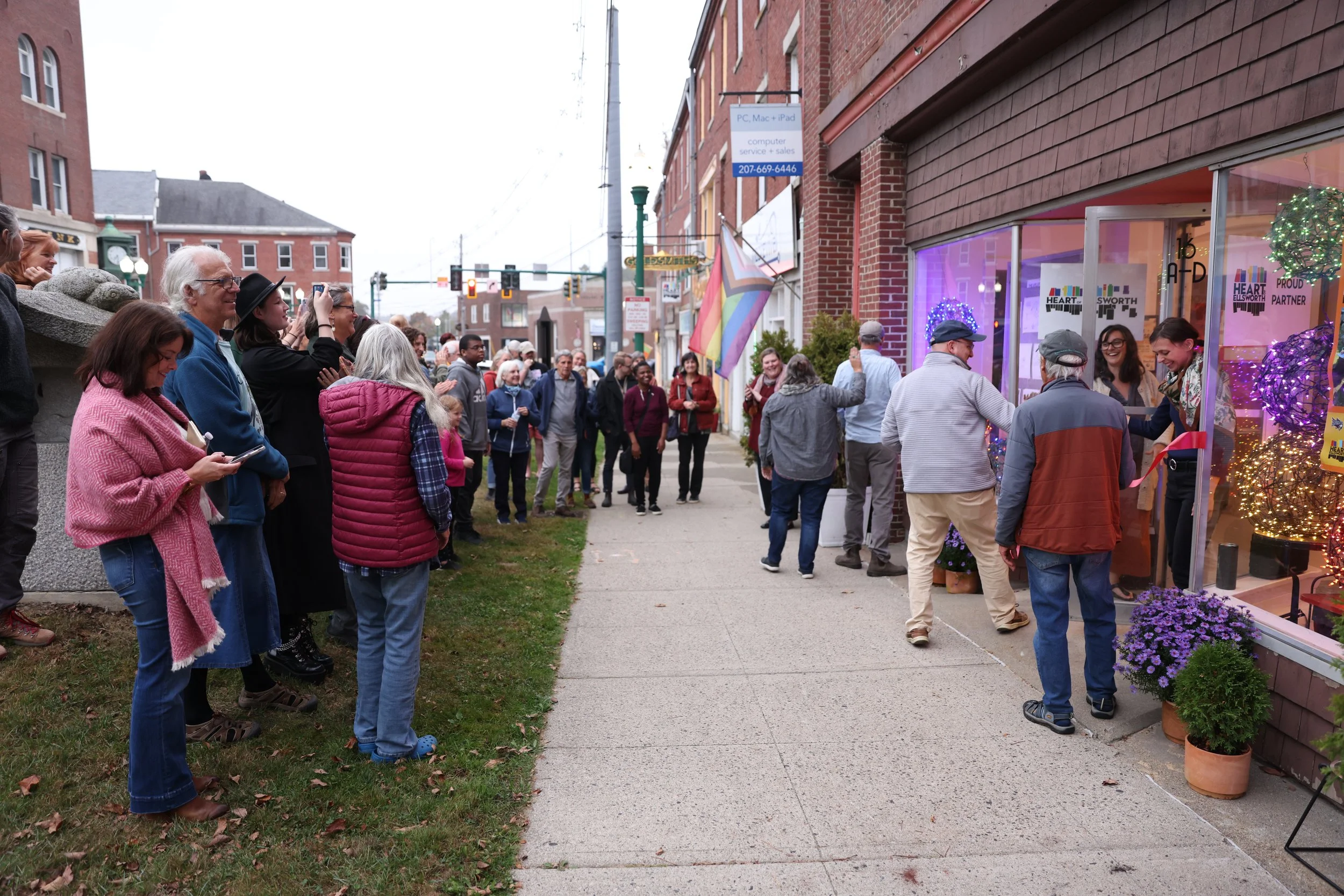 A crowd of people standing on a sidewalk outside a store decorated with colorful lights during a celebration or event.