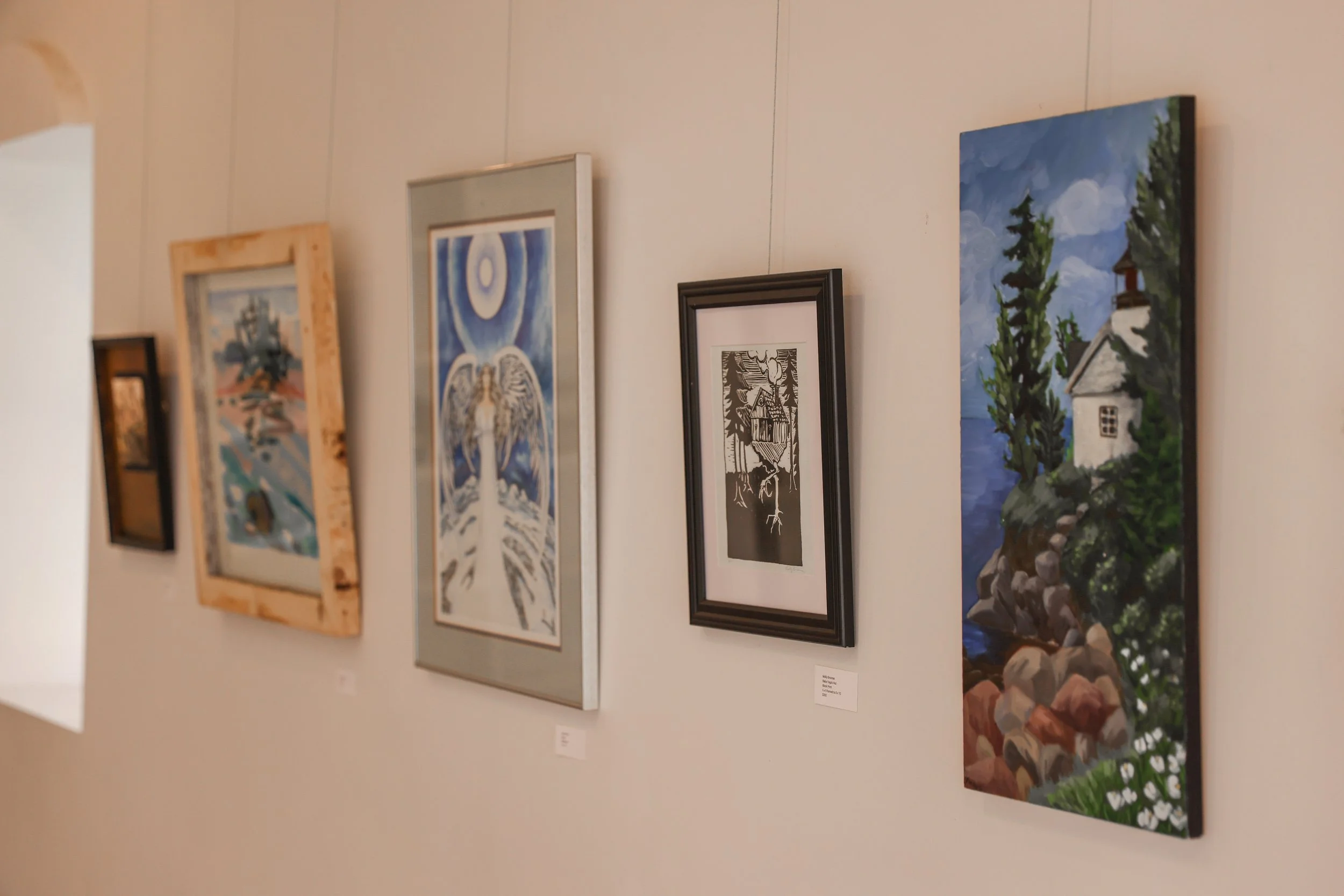 A wall in an art gallery displaying framed paintings and artwork.