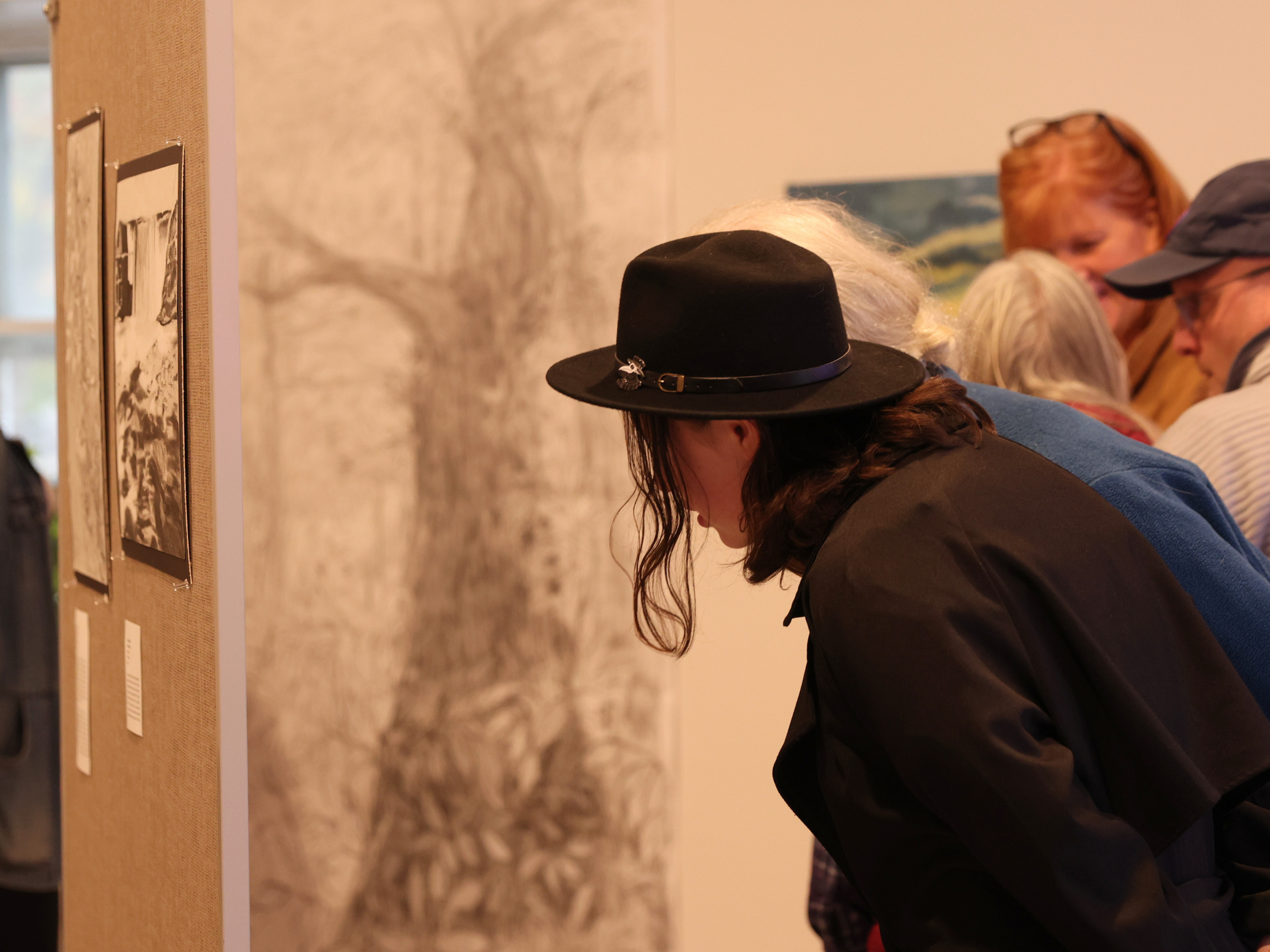 People viewing artwork or photographs on a display wall in an art gallery or museum.
