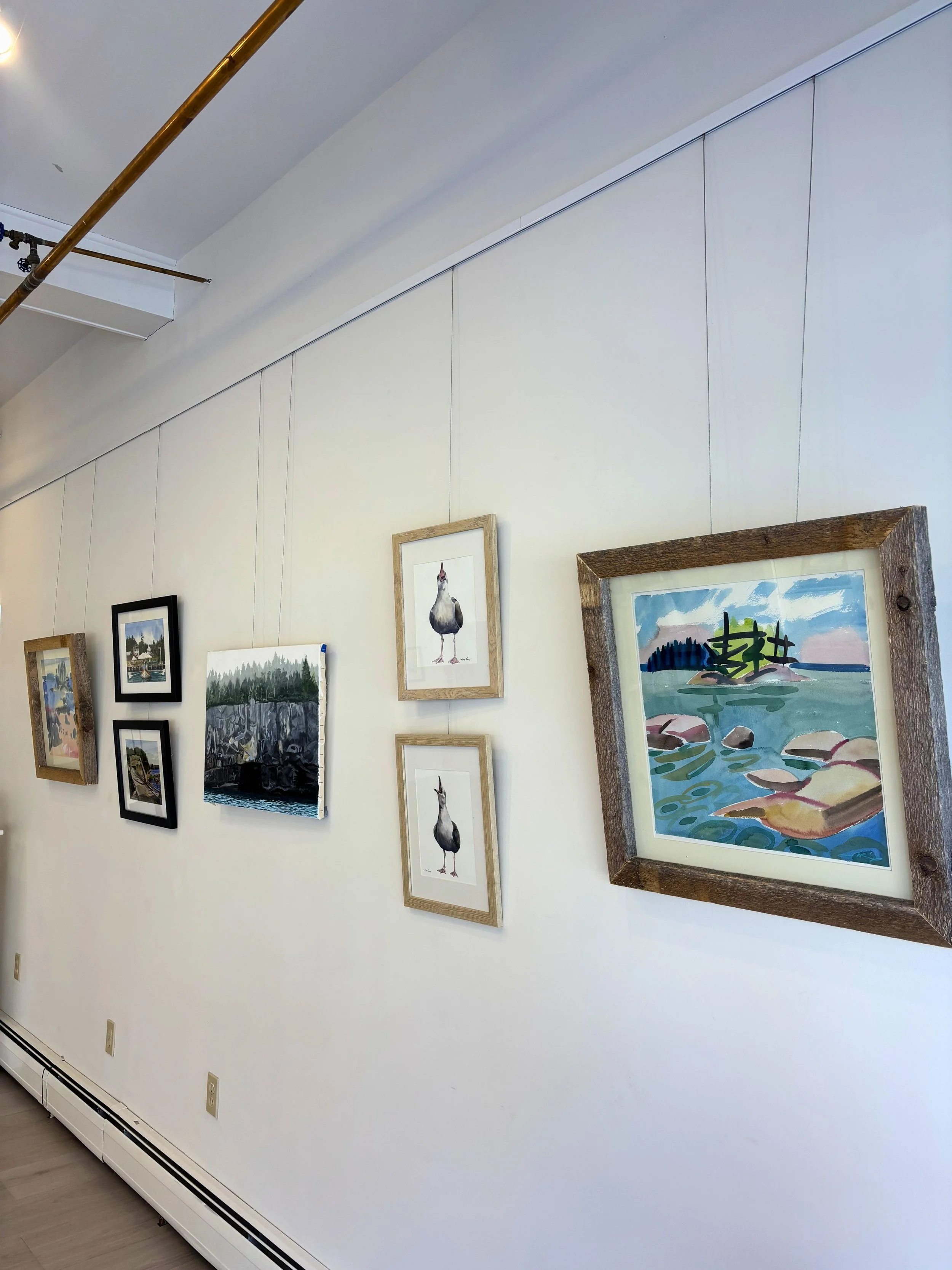 Wall with framed artwork including landscapes, birds, and nature scenes in an art gallery or exhibition space.