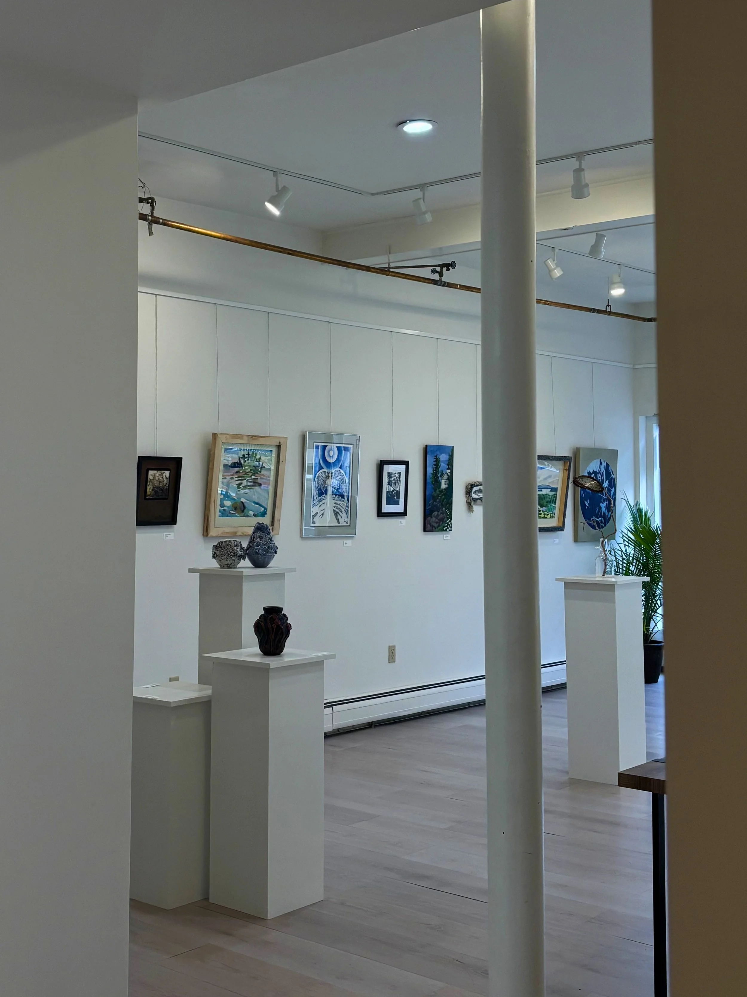 Art gallery with framed paintings on white walls and sculptures on white pedestals.