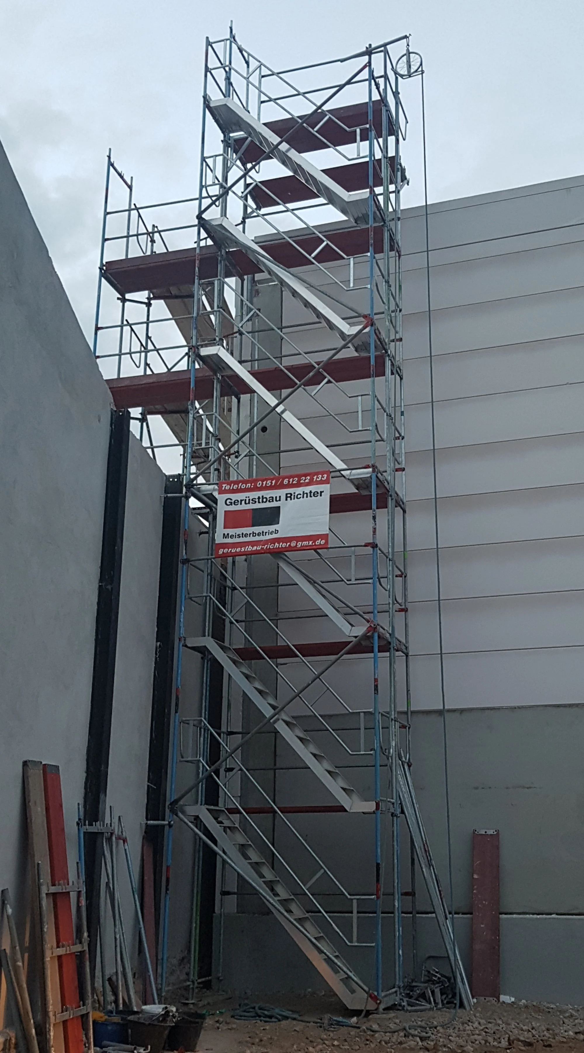 Gerüstbau auf einer Baustelle mit Aufstieg und Plattformen, am Gebäude angebracht, mit einem Schild, das die Firma Gerüstbau Richter anzeigt.