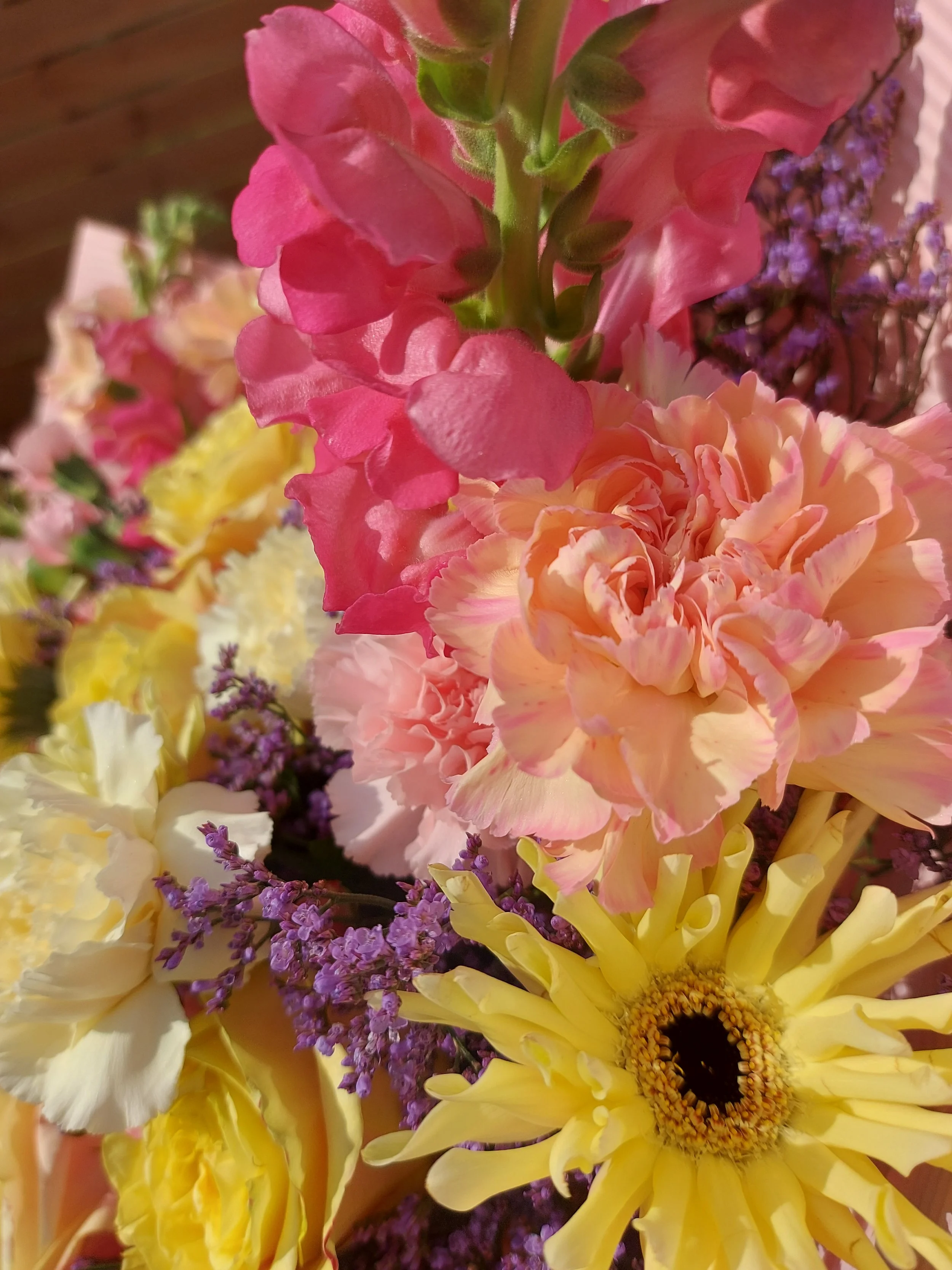 Close-up of a vibrant flower bouquet featuring a large yellow sunflower, pink and purple flowers, and various green foliage.