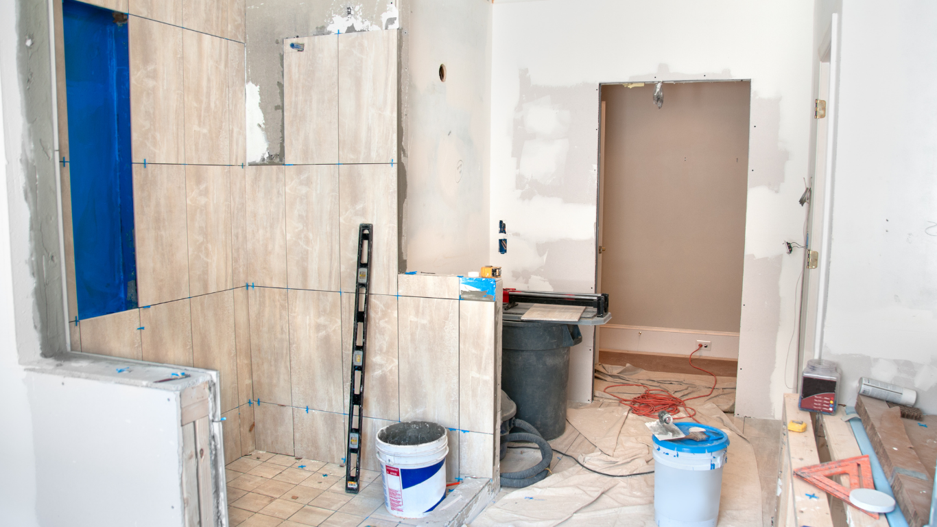 Bathroom under renovation with incomplete tile work, construction tools, and materials.