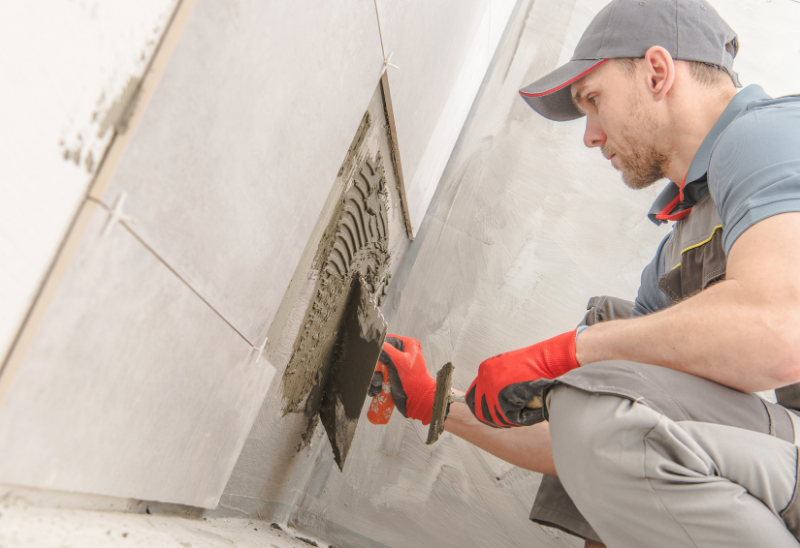 A worker laying tiles on a wall with a trowel.